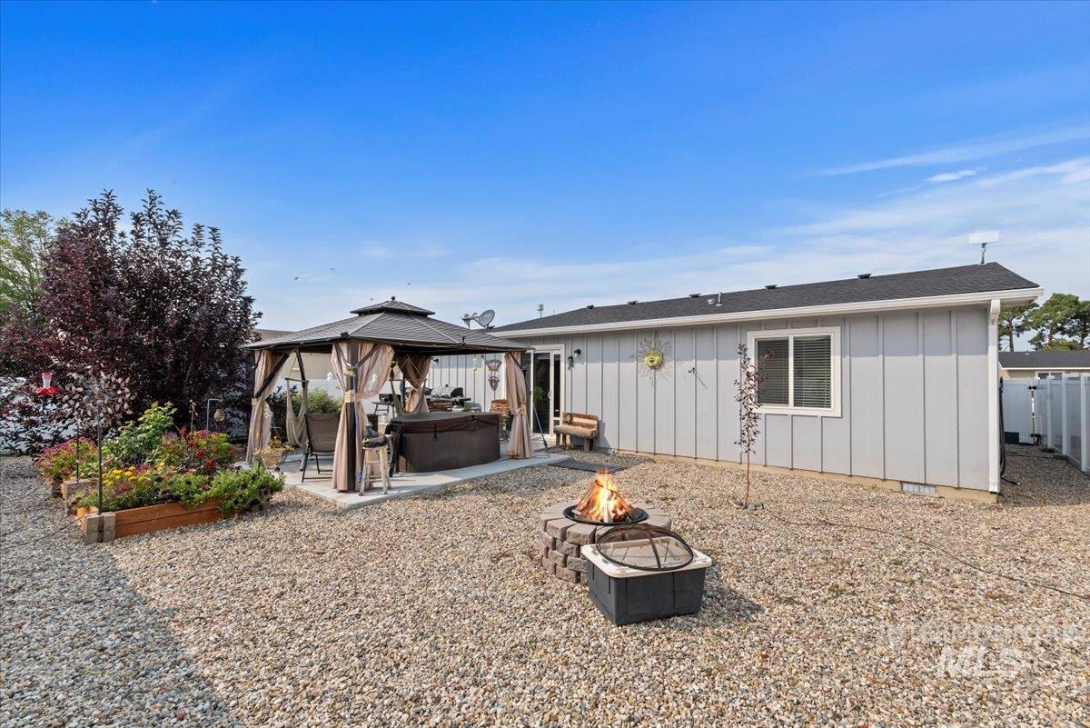 Rear view of property with a gazebo, board and batten siding, a patio, an outdoor fire pit, and a hot tub