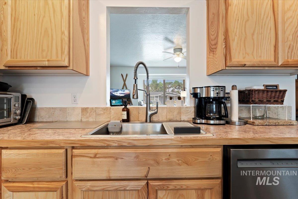 Kitchen with light brown cabinets, light countertops, stainless steel dishwasher, a ceiling fan, and a textured ceiling