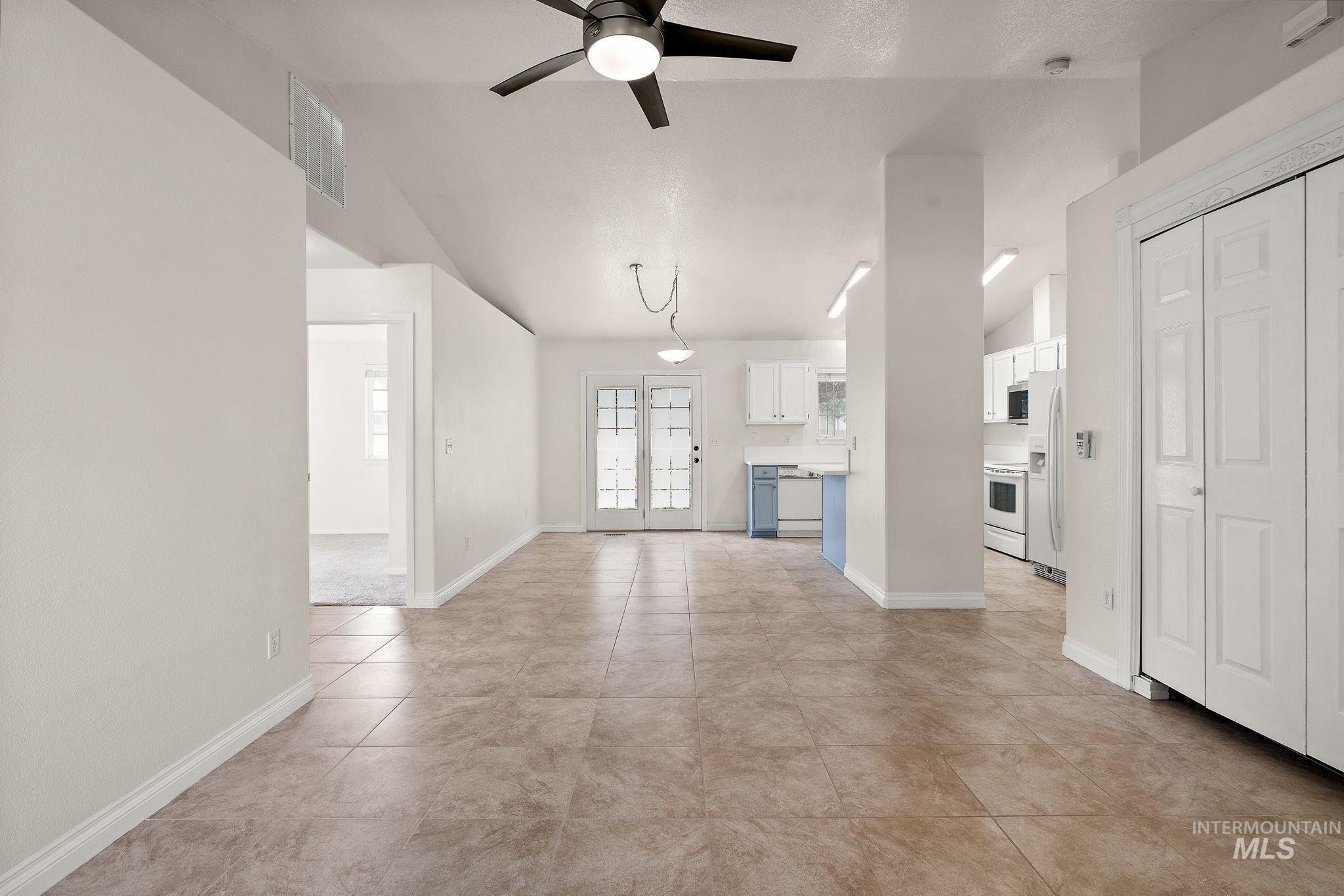 Unfurnished living room with vaulted ceiling, a ceiling fan, light tile patterned flooring, and french doors
