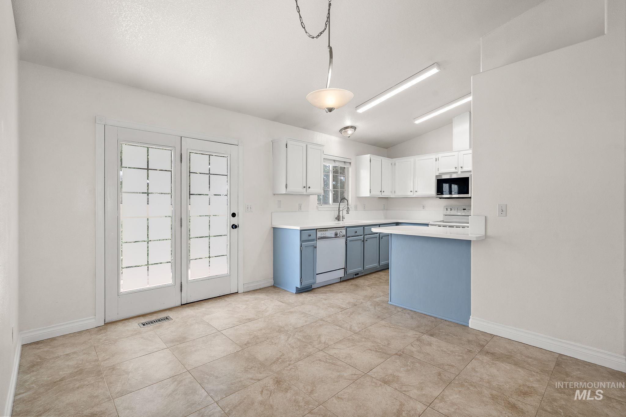 Kitchen featuring lofted ceiling, white cabinets, blue cabinets, light countertops, and pendant lighting