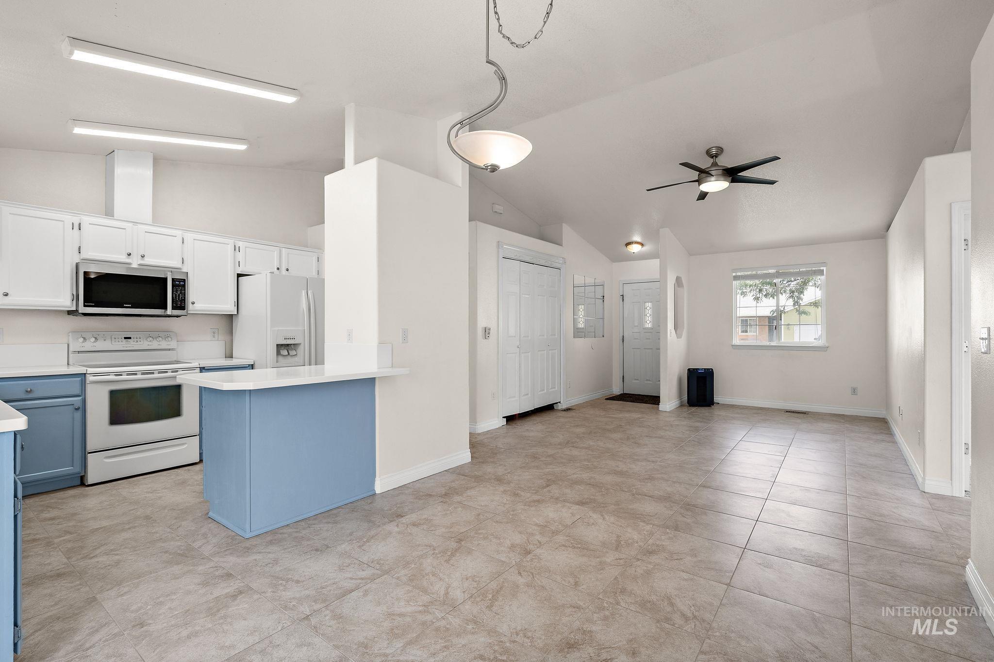 Kitchen featuring light countertops, white appliances, white cabinetry, blue cabinetry, and lofted ceiling