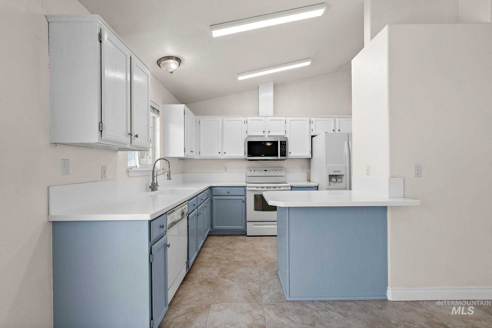 Kitchen featuring white cabinets, light countertops, lofted ceiling, white appliances, and blue cabinetry
