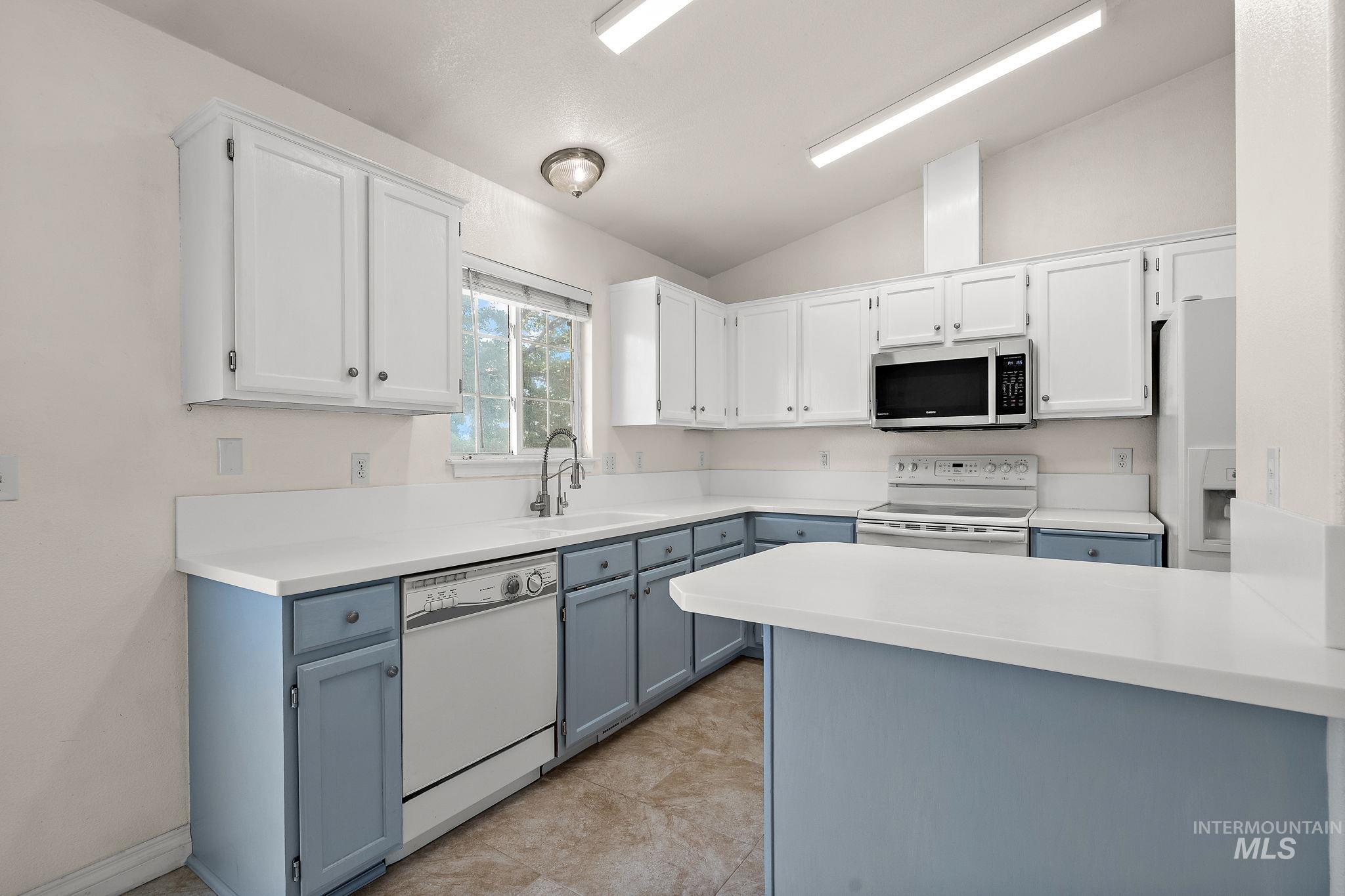 Kitchen featuring white cabinets, vaulted ceiling, white appliances, a peninsula, and blue cabinetry