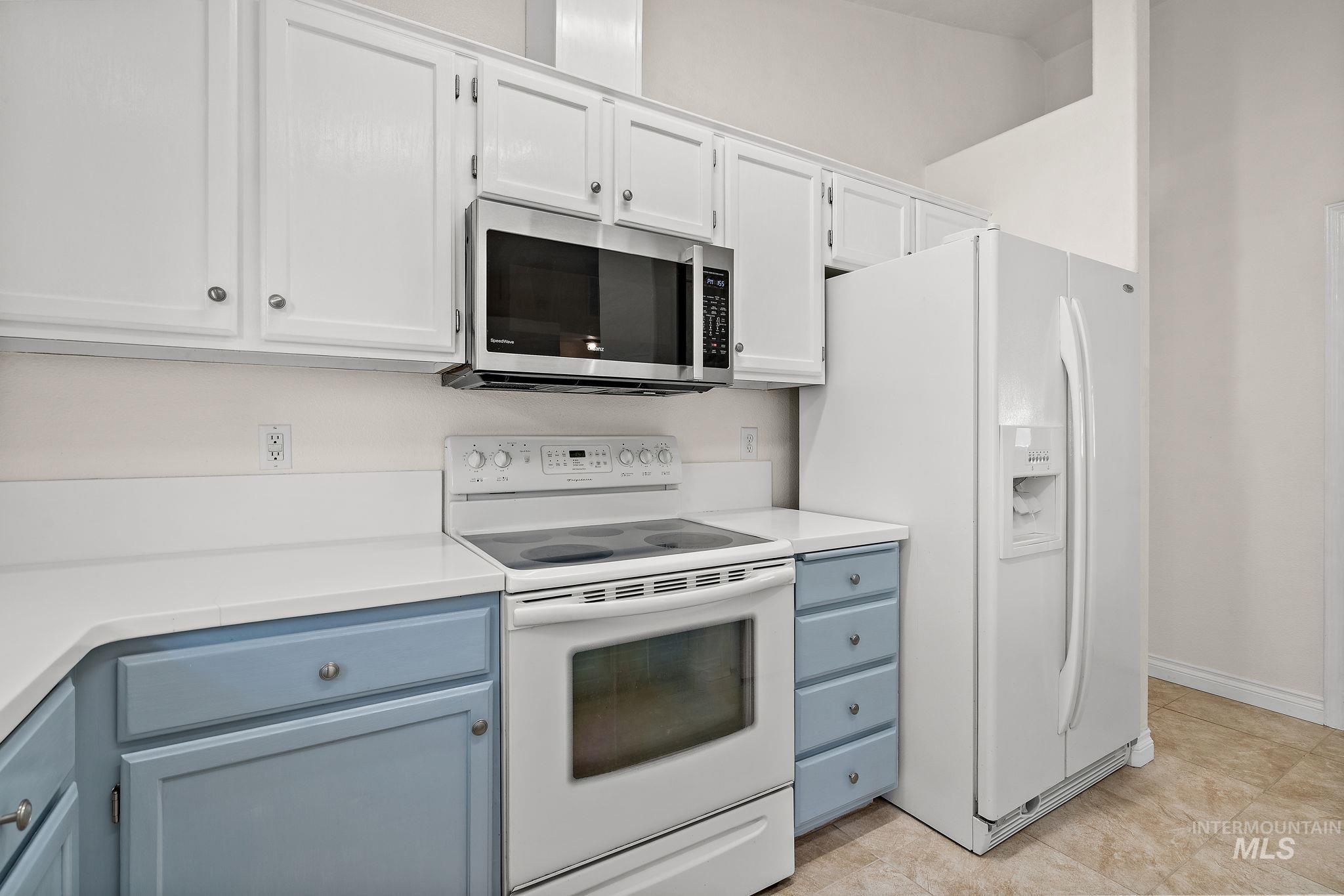 Kitchen featuring white appliances, white cabinetry, light tile patterned flooring, and blue cabinetry