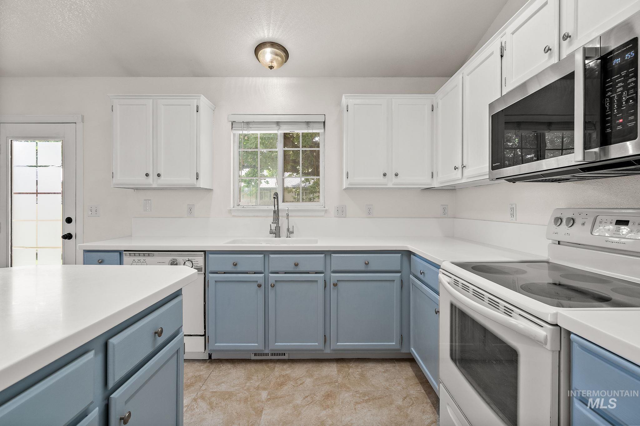 Kitchen featuring white appliances, white cabinets, light countertops, and blue cabinetry