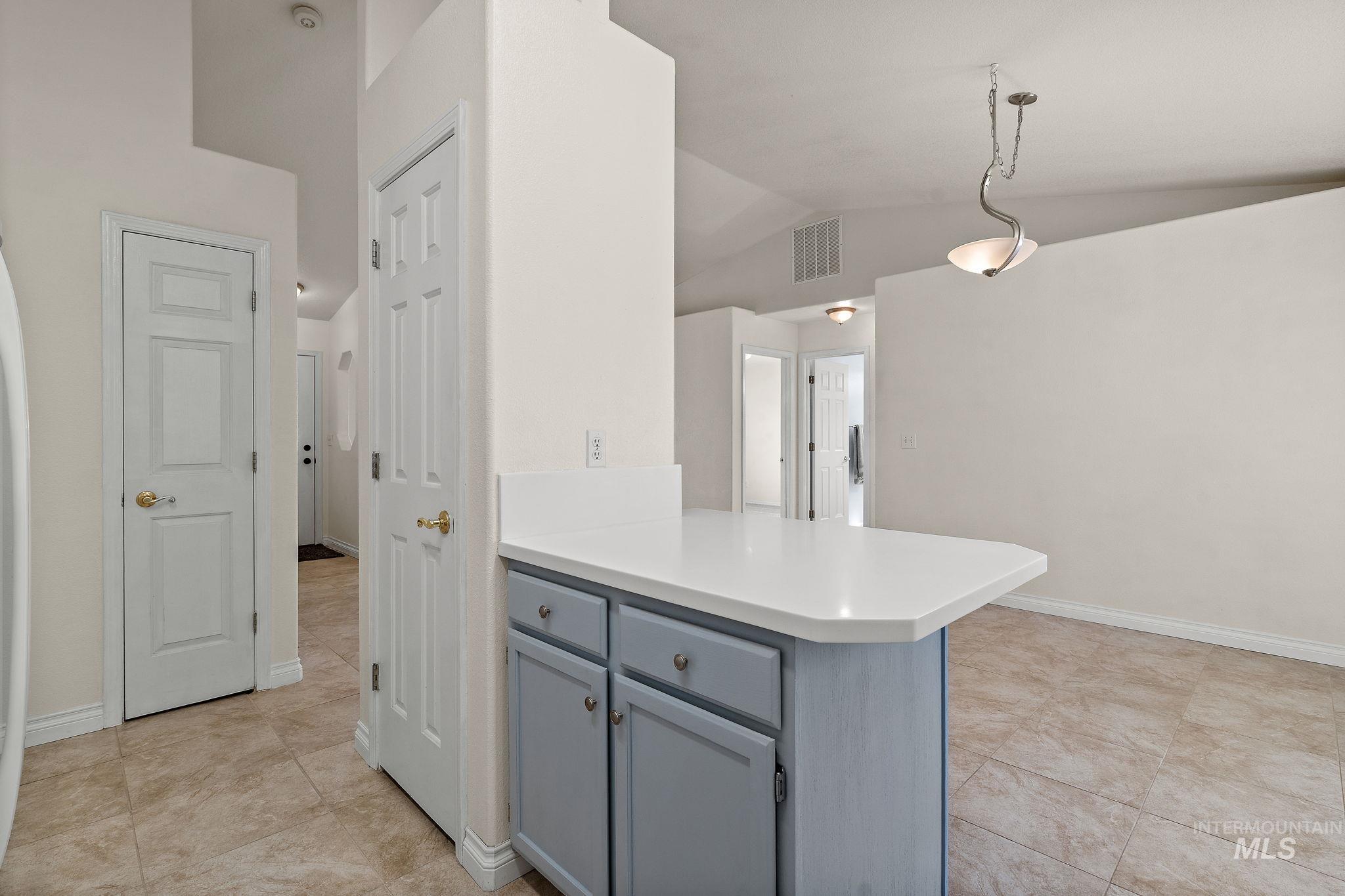 Kitchen featuring a peninsula, vaulted ceiling, gray cabinetry, light countertops, and decorative light fixtures