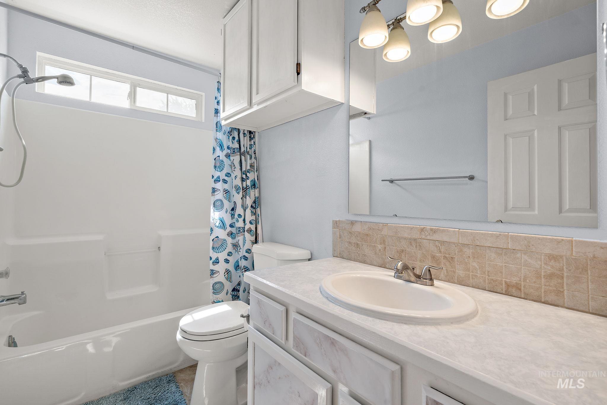 Bathroom with shower / bath combo, vanity, and tasteful backsplash