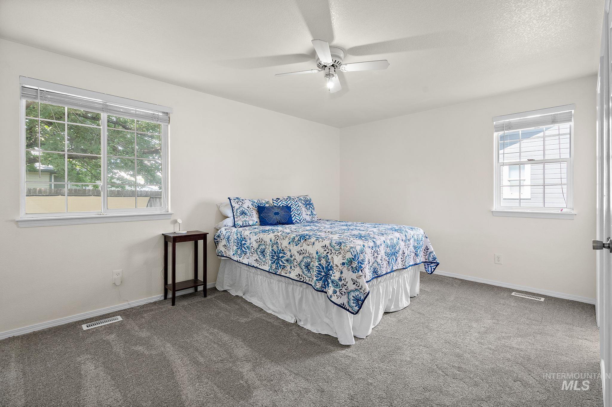 Carpeted bedroom featuring ceiling fan and multiple windows