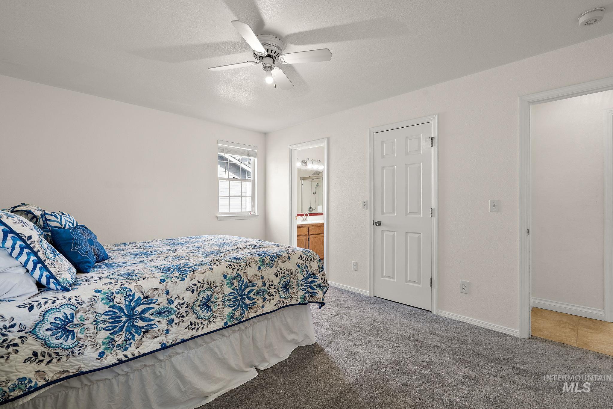 Carpeted bedroom featuring ensuite bath and a ceiling fan