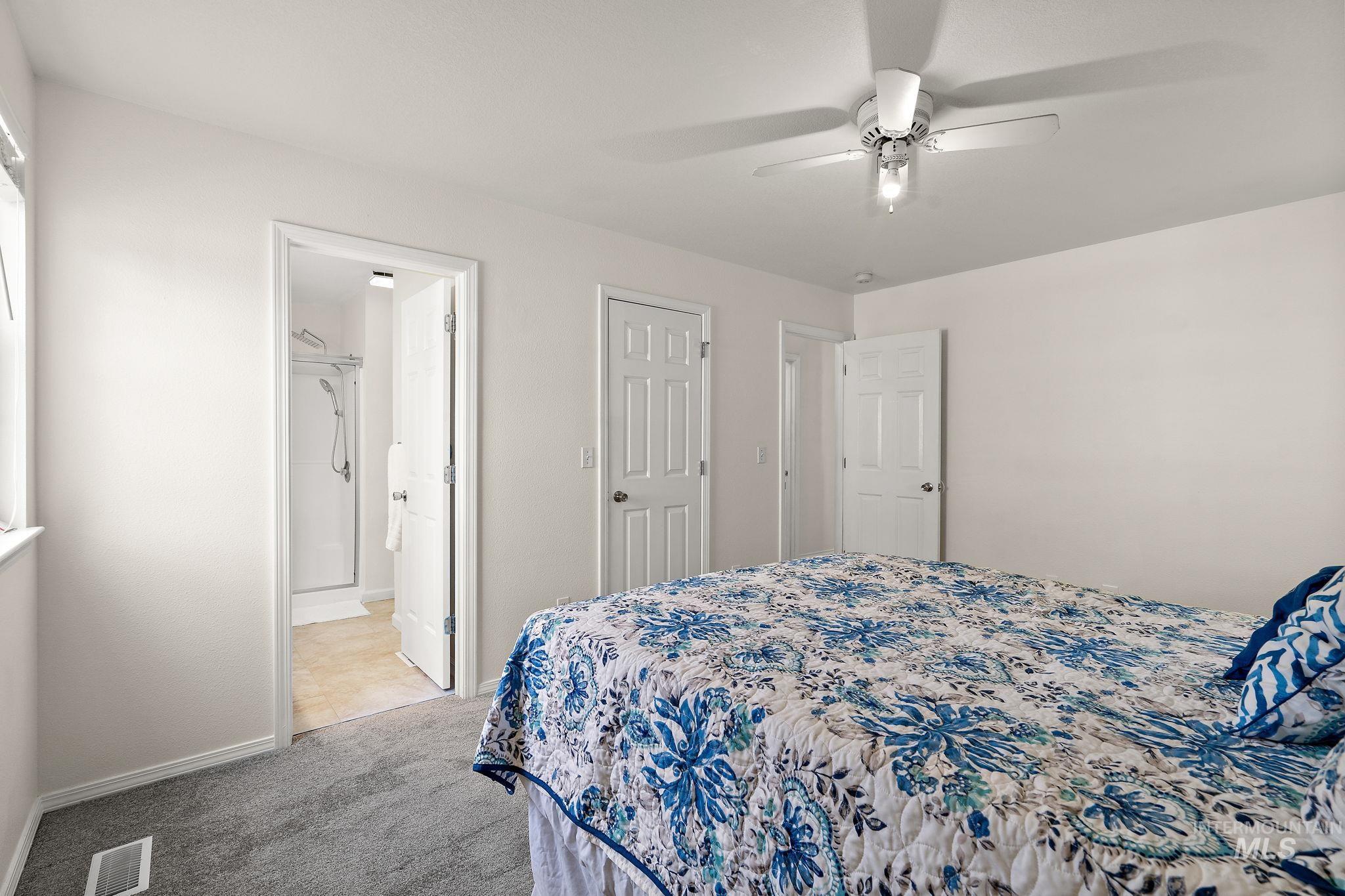 Bedroom with light colored carpet, ceiling fan, and ensuite bathroom