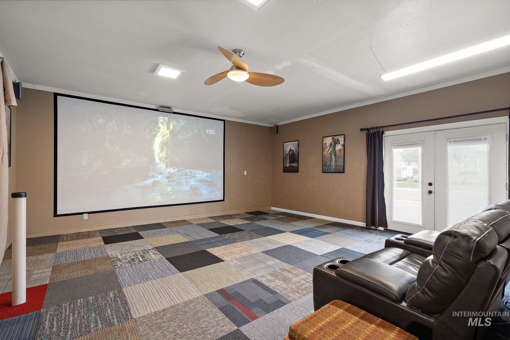 Carpeted home theater room with ceiling fan and french doors