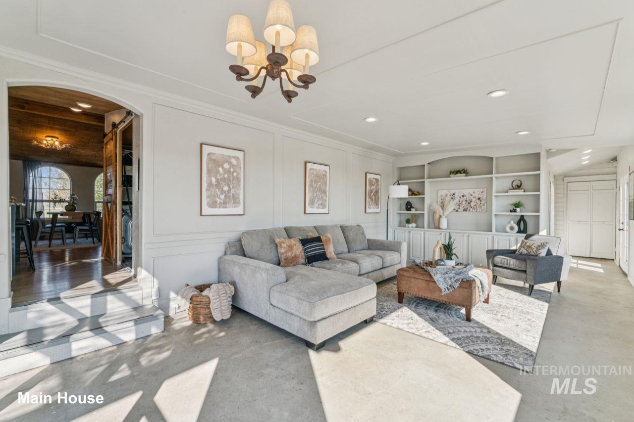 Living room with a decorative wall, a chandelier, arched walkways, concrete flooring, and built in shelves