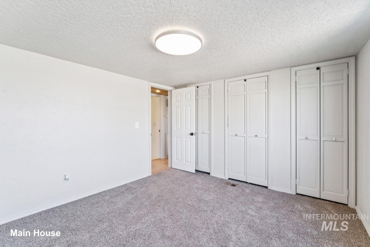 Unfurnished bedroom with two closets, a textured ceiling, and light colored carpet