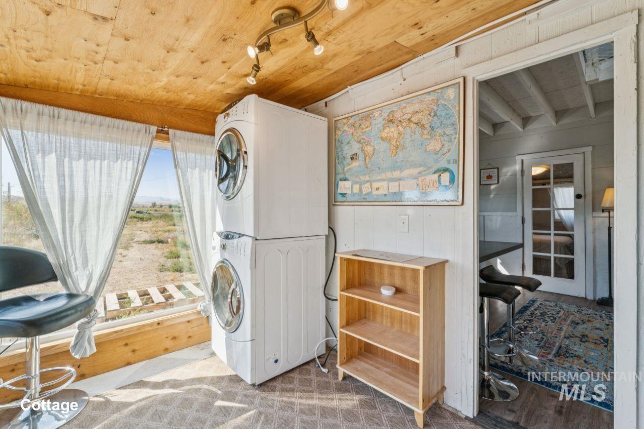 Laundry room featuring stacked washing machine and dryer, wood finished floors, wooden ceiling, and wood walls