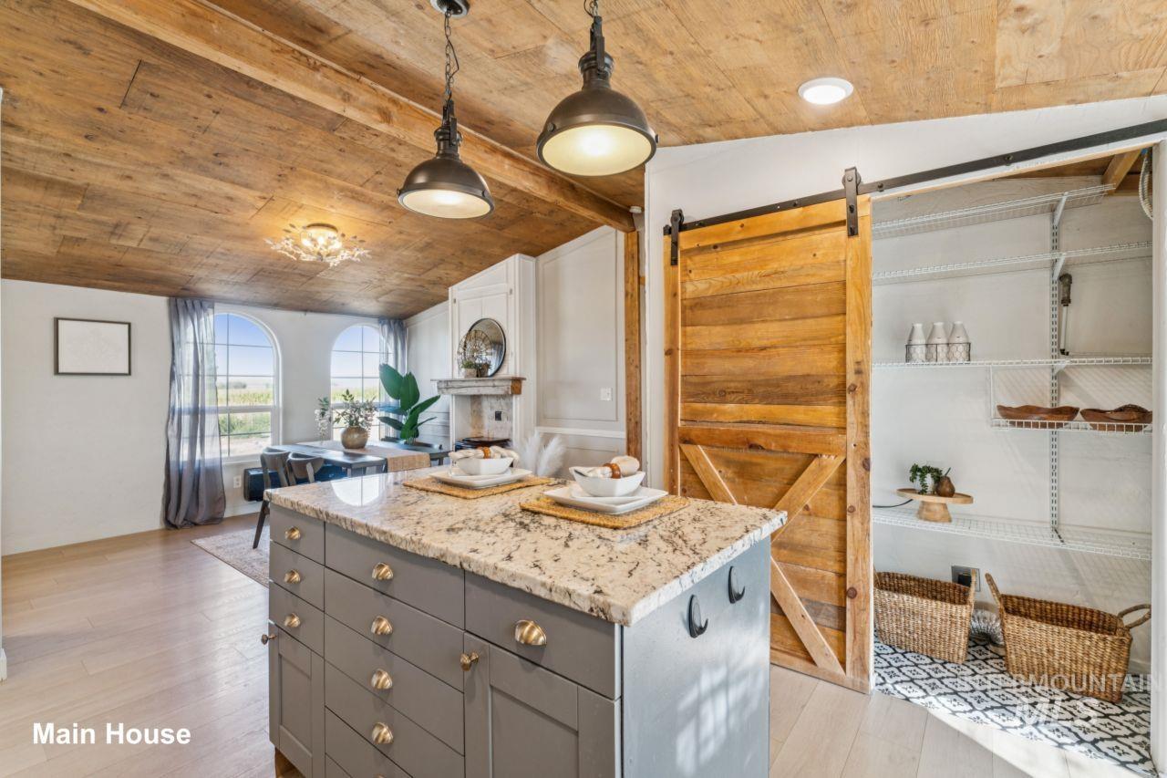 Kitchen with gray cabinetry, hanging light fixtures, a barn door, light stone counters, and light wood-style flooring