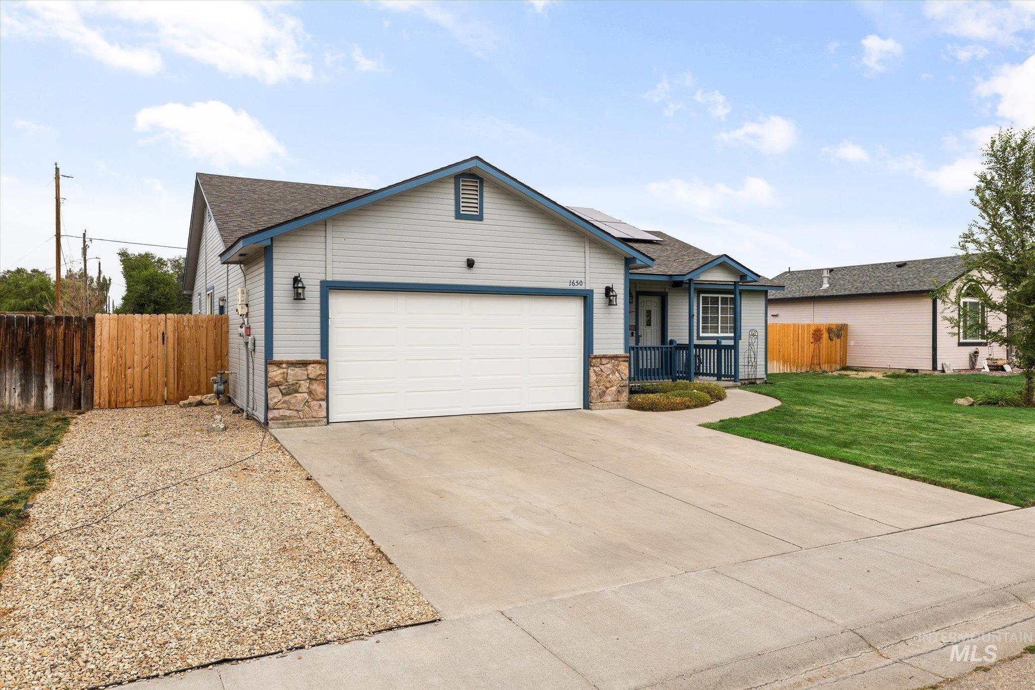 Ranch-style house with stone siding, roof mounted solar panels, roof with shingles, and concrete driveway