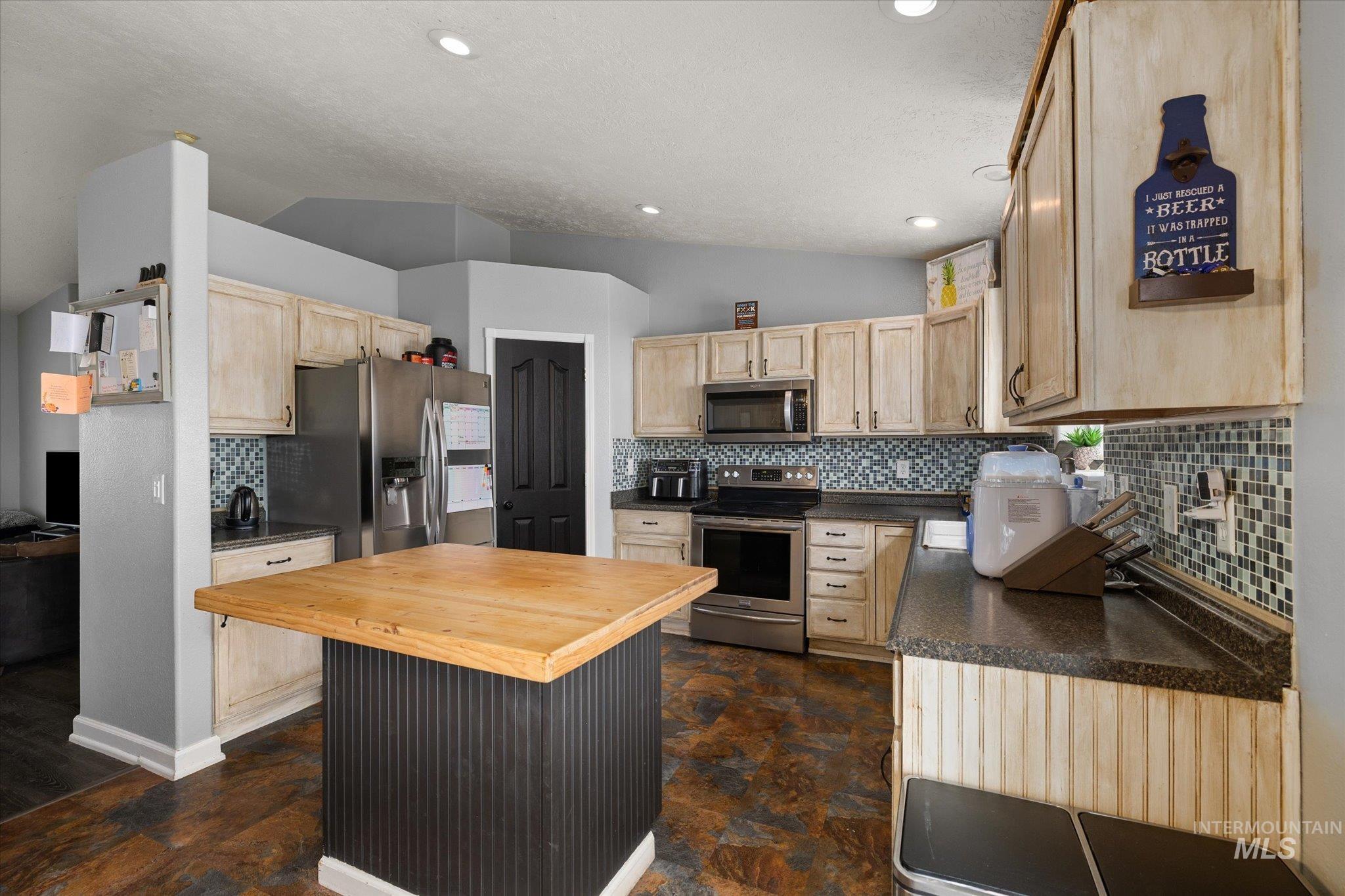 Kitchen featuring vaulted ceiling, light brown cabinetry, backsplash, appliances with stainless steel finishes, and butcher block countertops