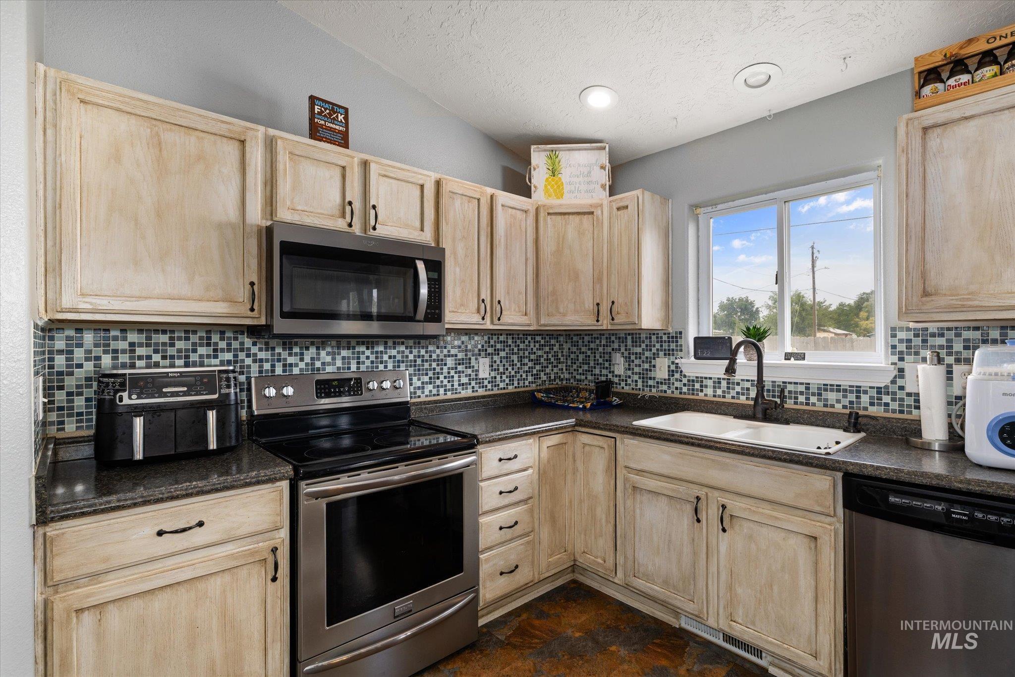 Kitchen with light brown cabinets, stainless steel appliances, dark countertops, a textured ceiling, and recessed lighting