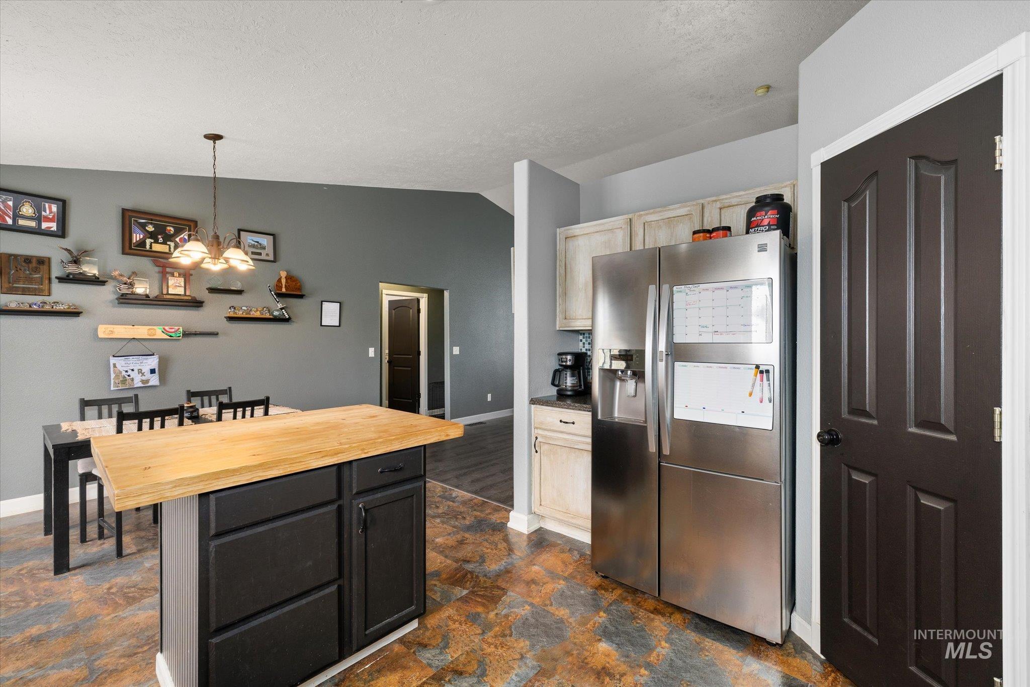 Kitchen with vaulted ceiling, stainless steel fridge, butcher block counters, decorative light fixtures, and a chandelier