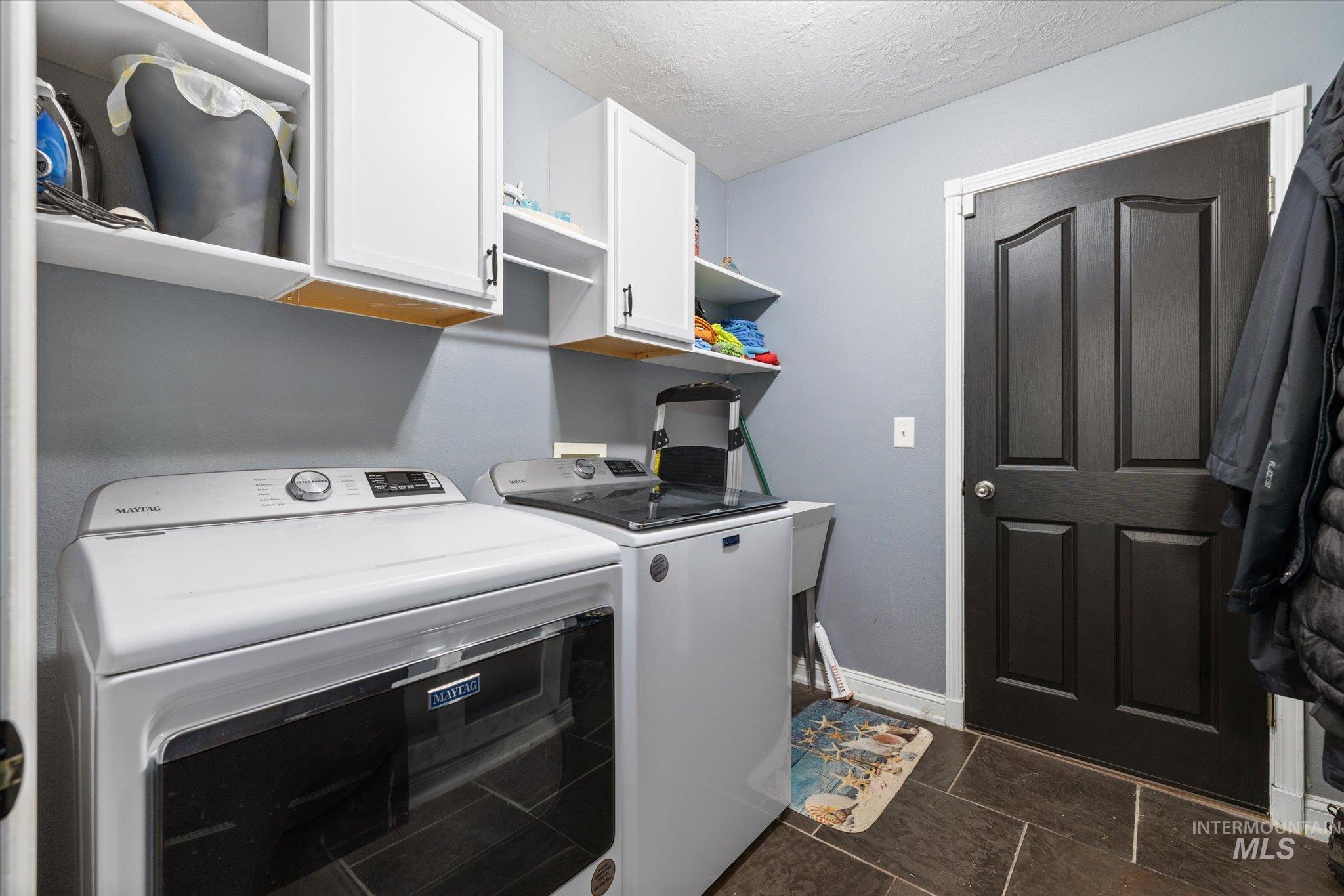 Laundry room with cabinet space, a textured ceiling, and washer and clothes dryer