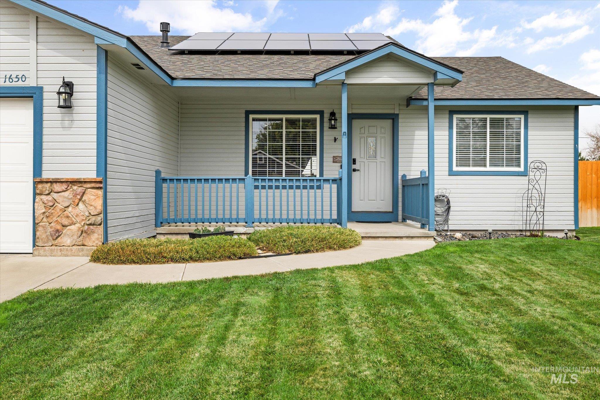 View of front facade with roof with shingles, a front lawn, and solar panels