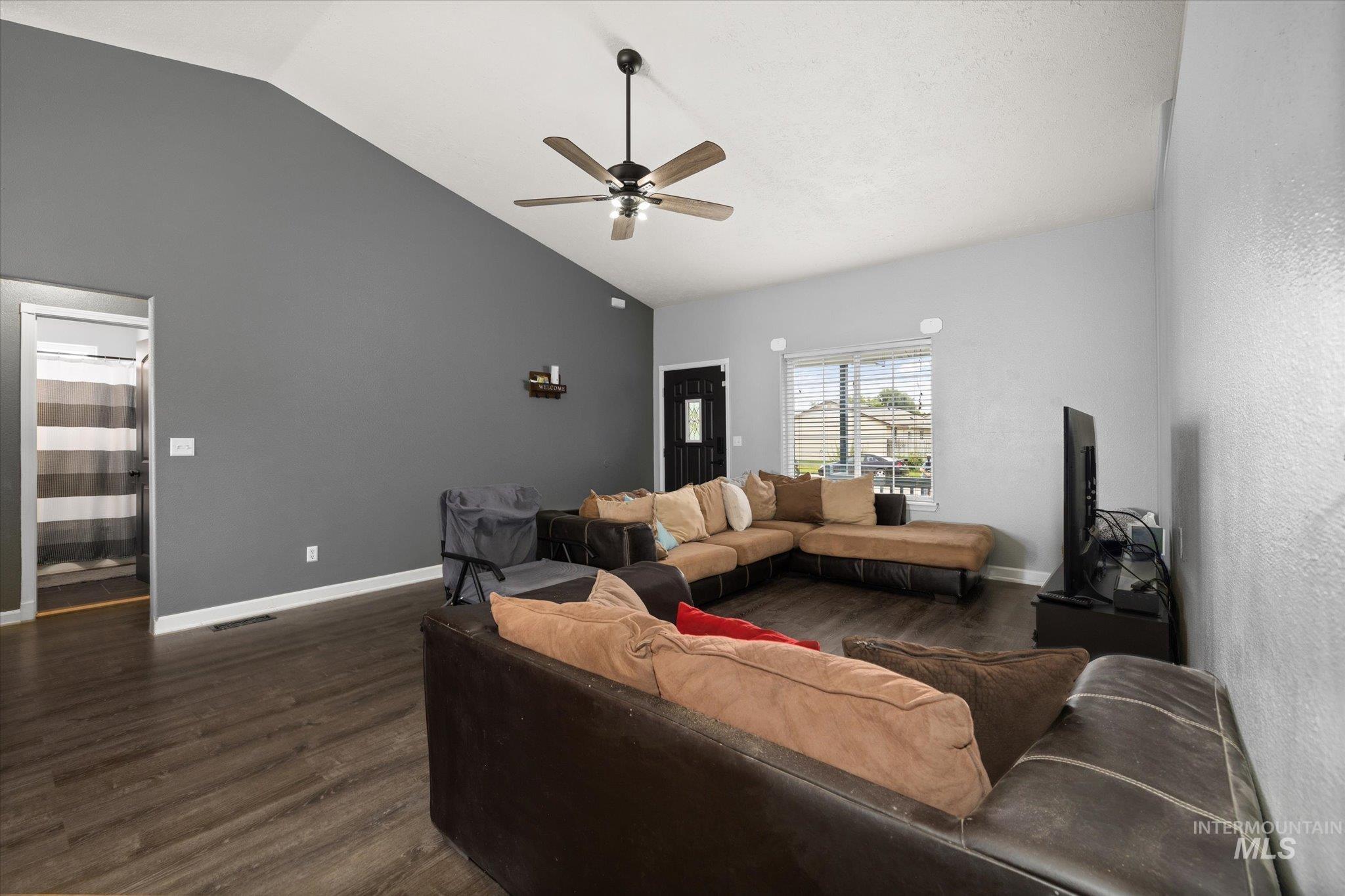 Living area with dark wood-style floors, ceiling fan, and high vaulted ceiling