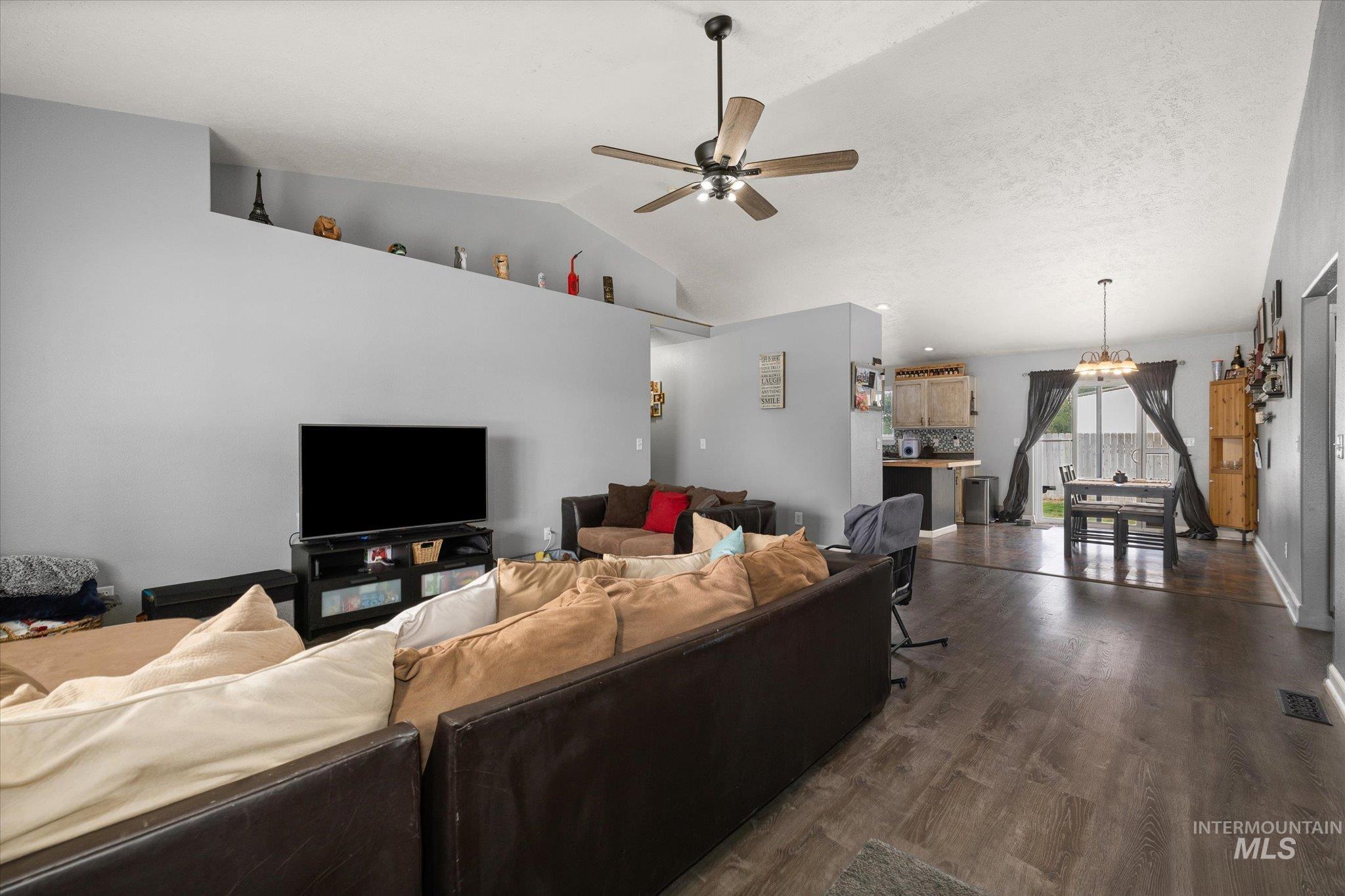 Living area with dark wood-style flooring, vaulted ceiling, and a ceiling fan
