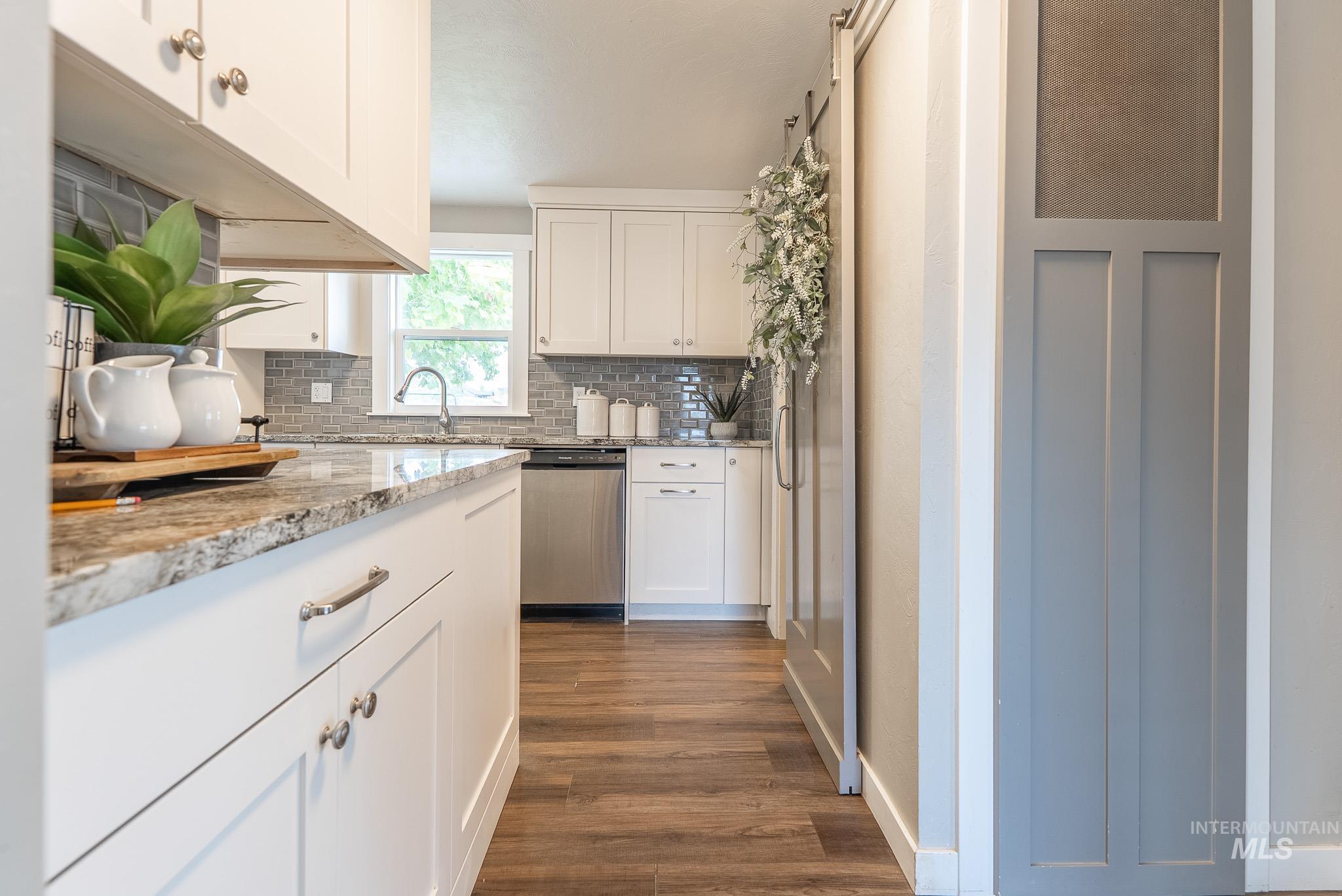 Kitchen featuring light stone countertops, dark wood-style flooring, dishwasher, and white cabinetry