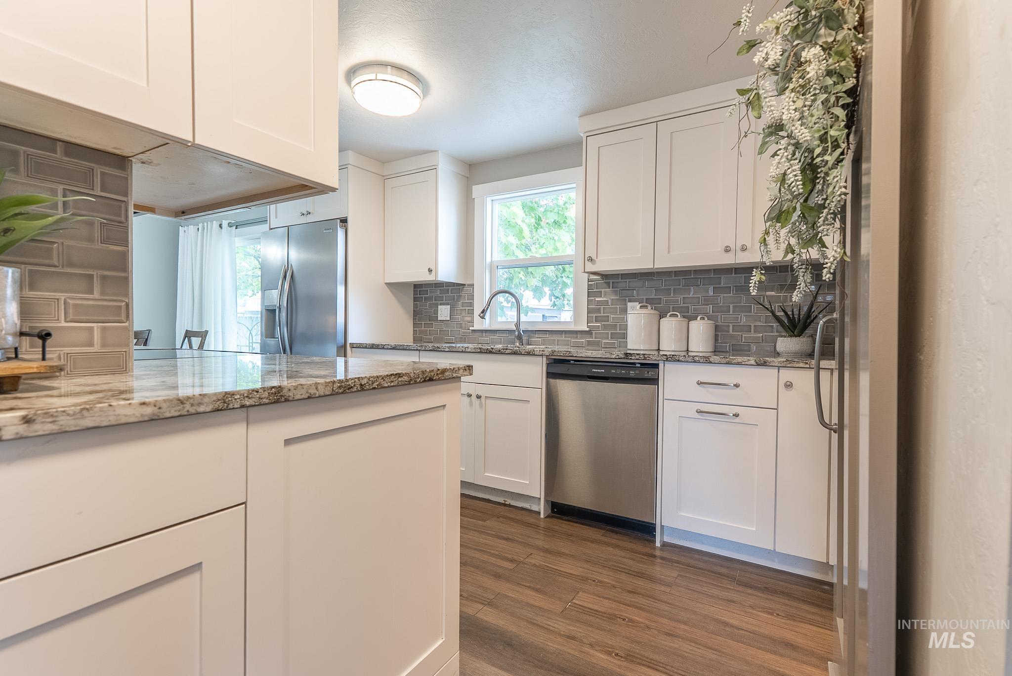 Kitchen with light stone countertops, stainless steel appliances, white cabinets, decorative backsplash, and dark wood-type flooring