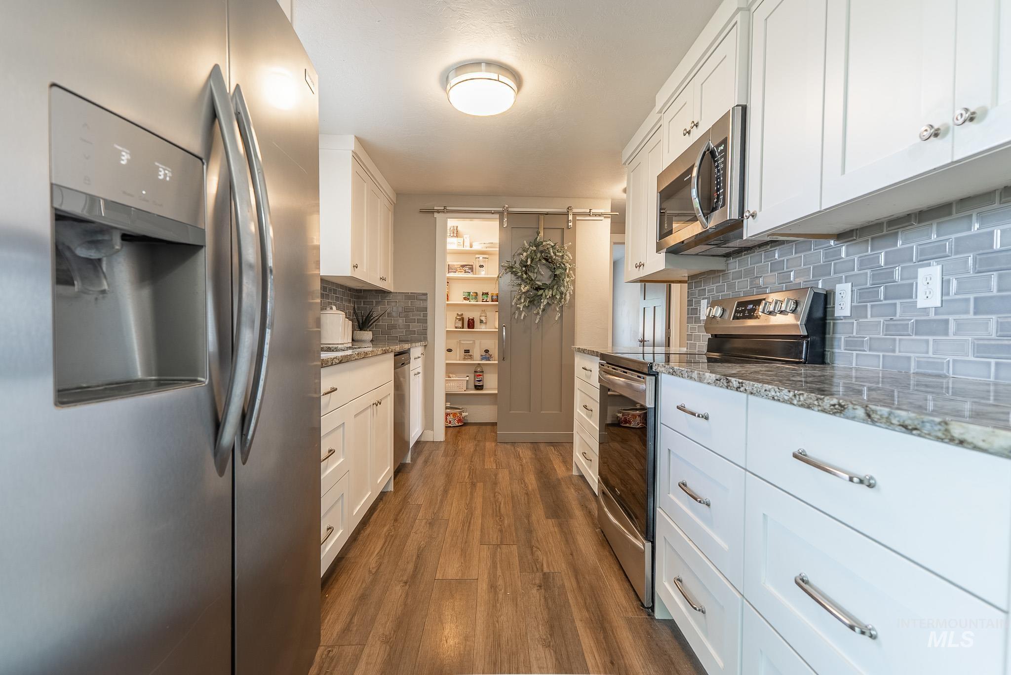 Kitchen featuring appliances with stainless steel finishes, light stone counters, dark wood-type flooring, and white cabinets