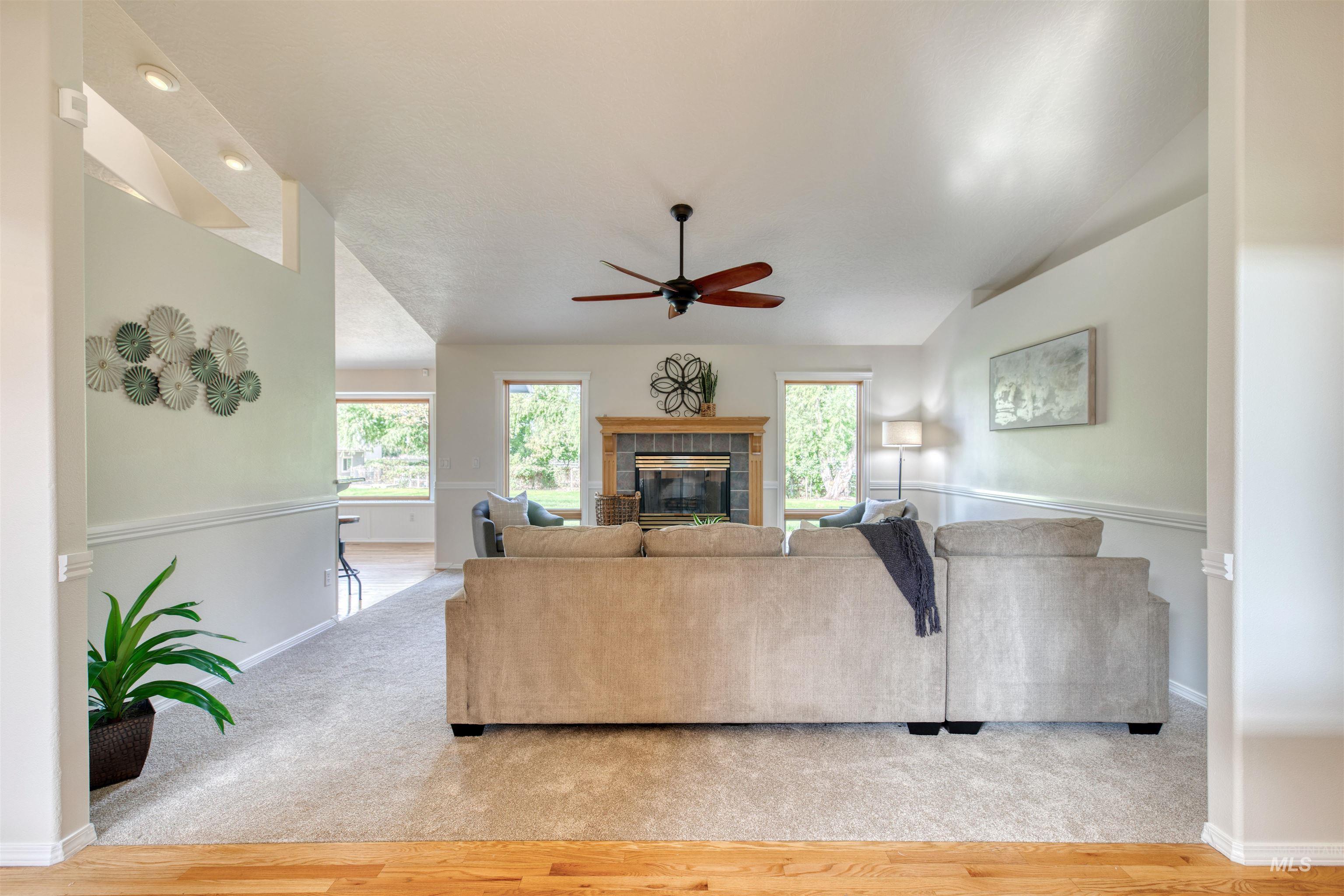 Living area featuring a fireplace, a ceiling fan, light colored carpet, vaulted ceiling, and light wood finished floors