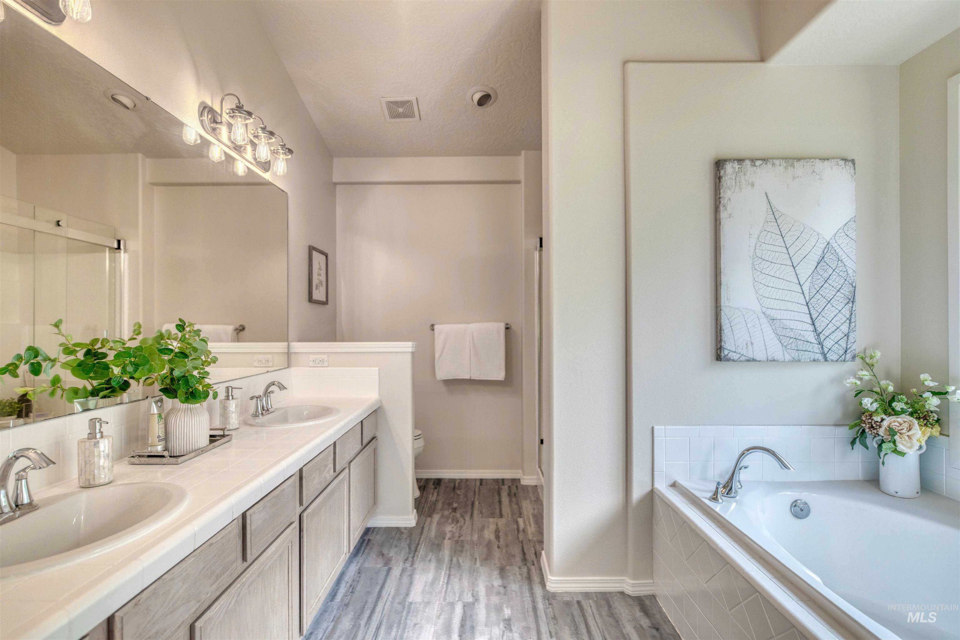 Full bathroom with a garden tub, double vanity, a shower stall, light wood-type flooring, and a textured ceiling