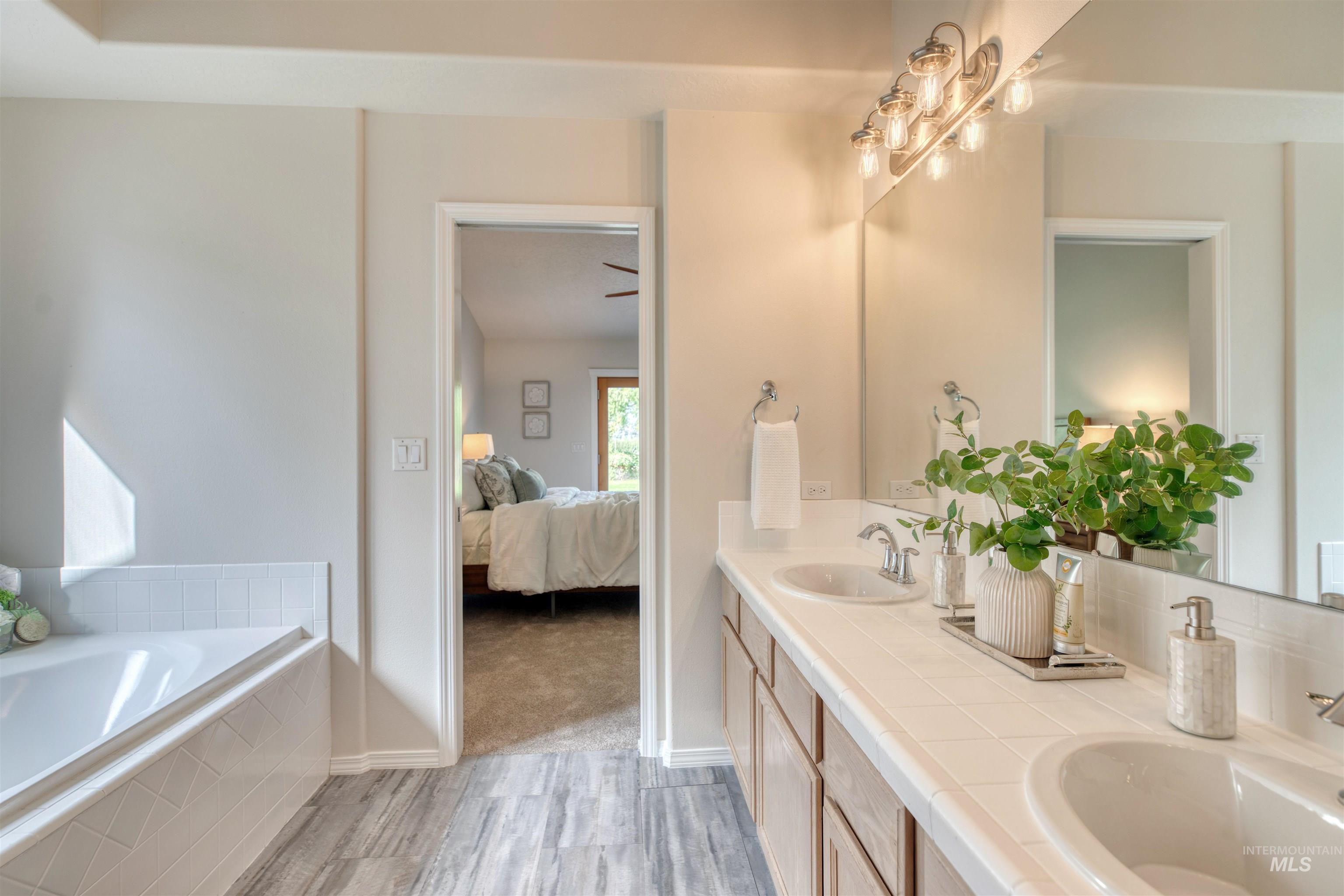 Full bathroom featuring ensuite bathroom, double vanity, a garden tub, and light wood-type flooring