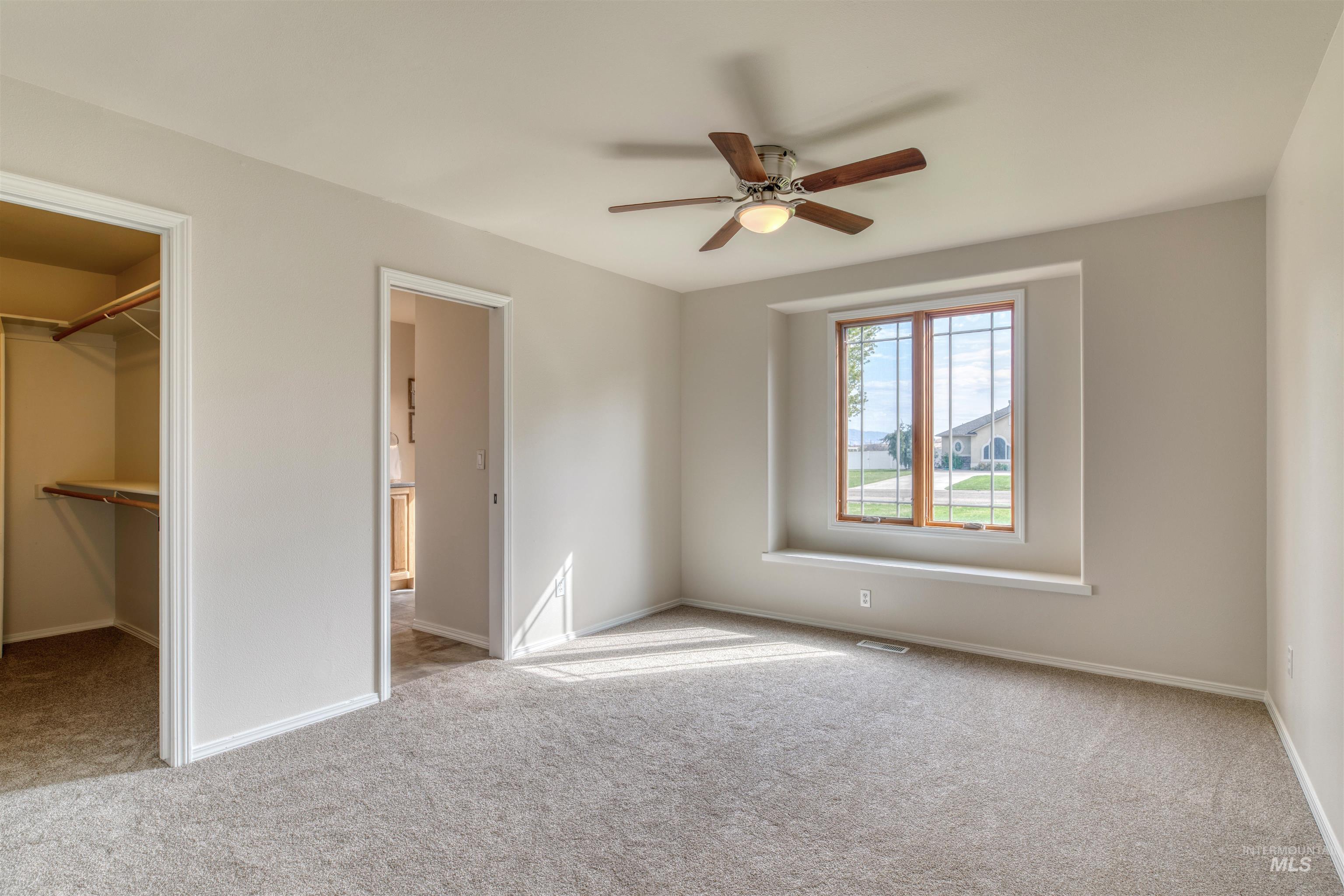 Unfurnished bedroom with light carpet, a spacious closet, and a ceiling fan