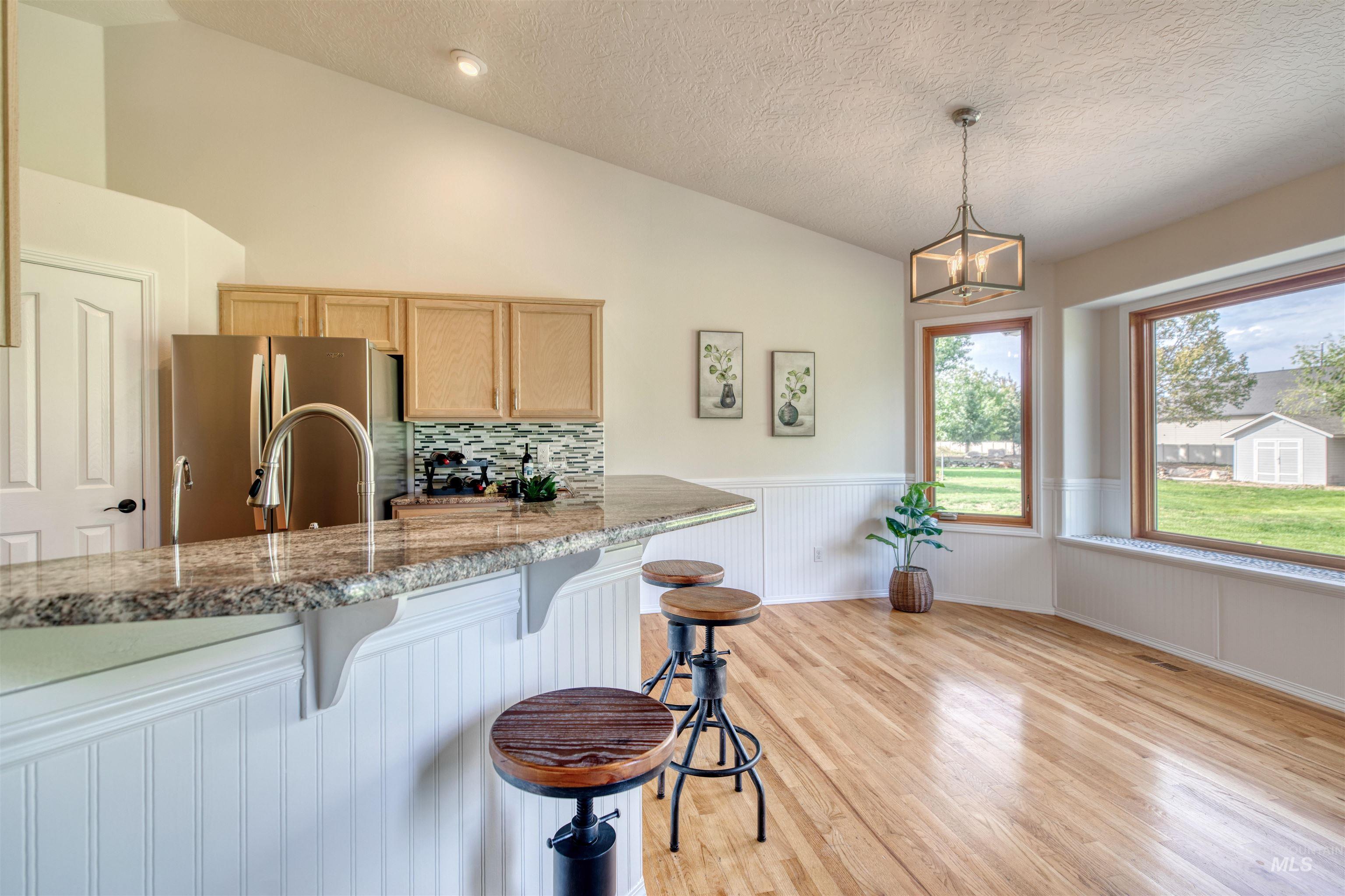 Kitchen featuring light stone countertops, vaulted ceiling, light wood-type flooring, decorative backsplash, and a kitchen bar