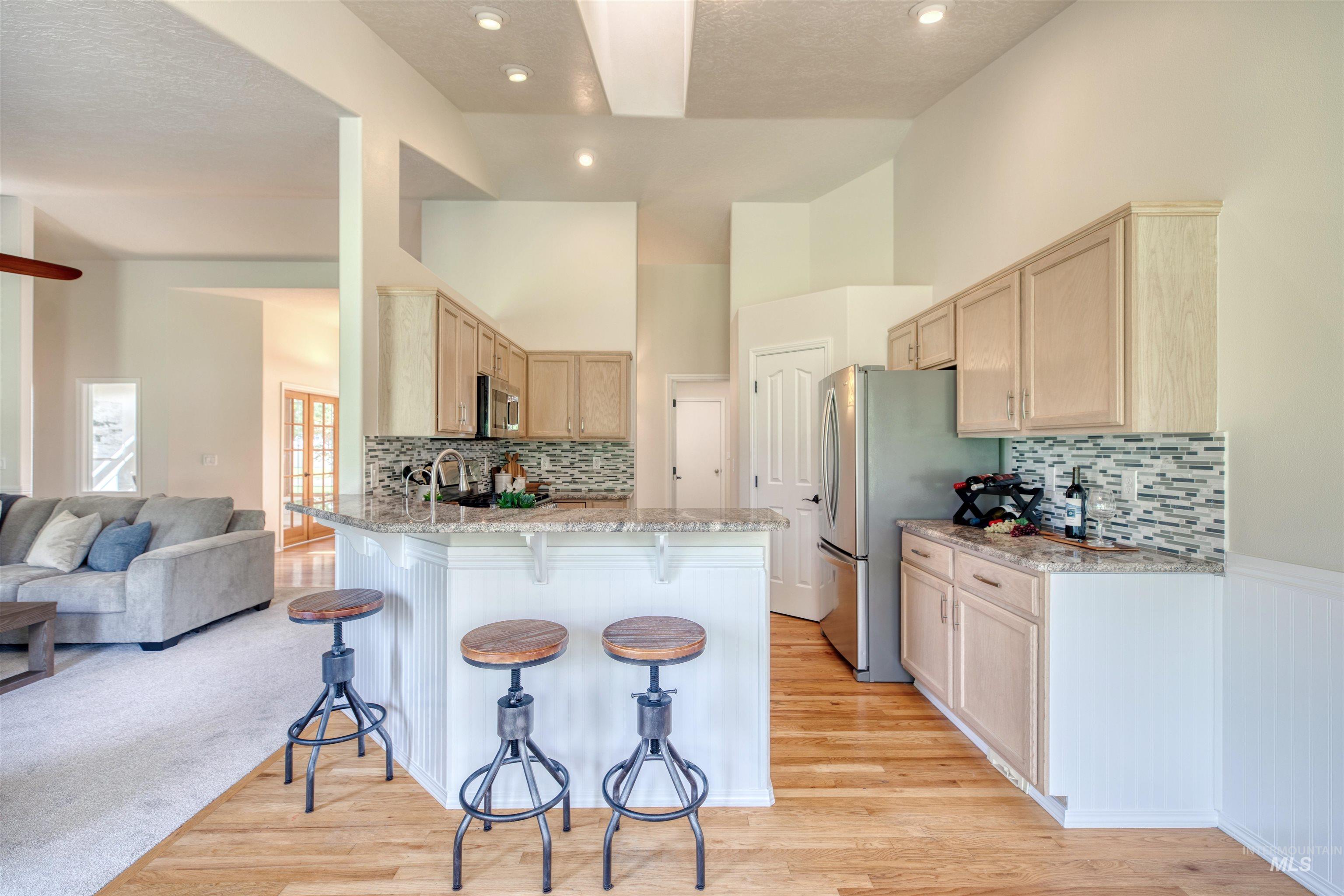 Kitchen with light brown cabinets, a breakfast bar, light stone counters, a peninsula, and decorative backsplash