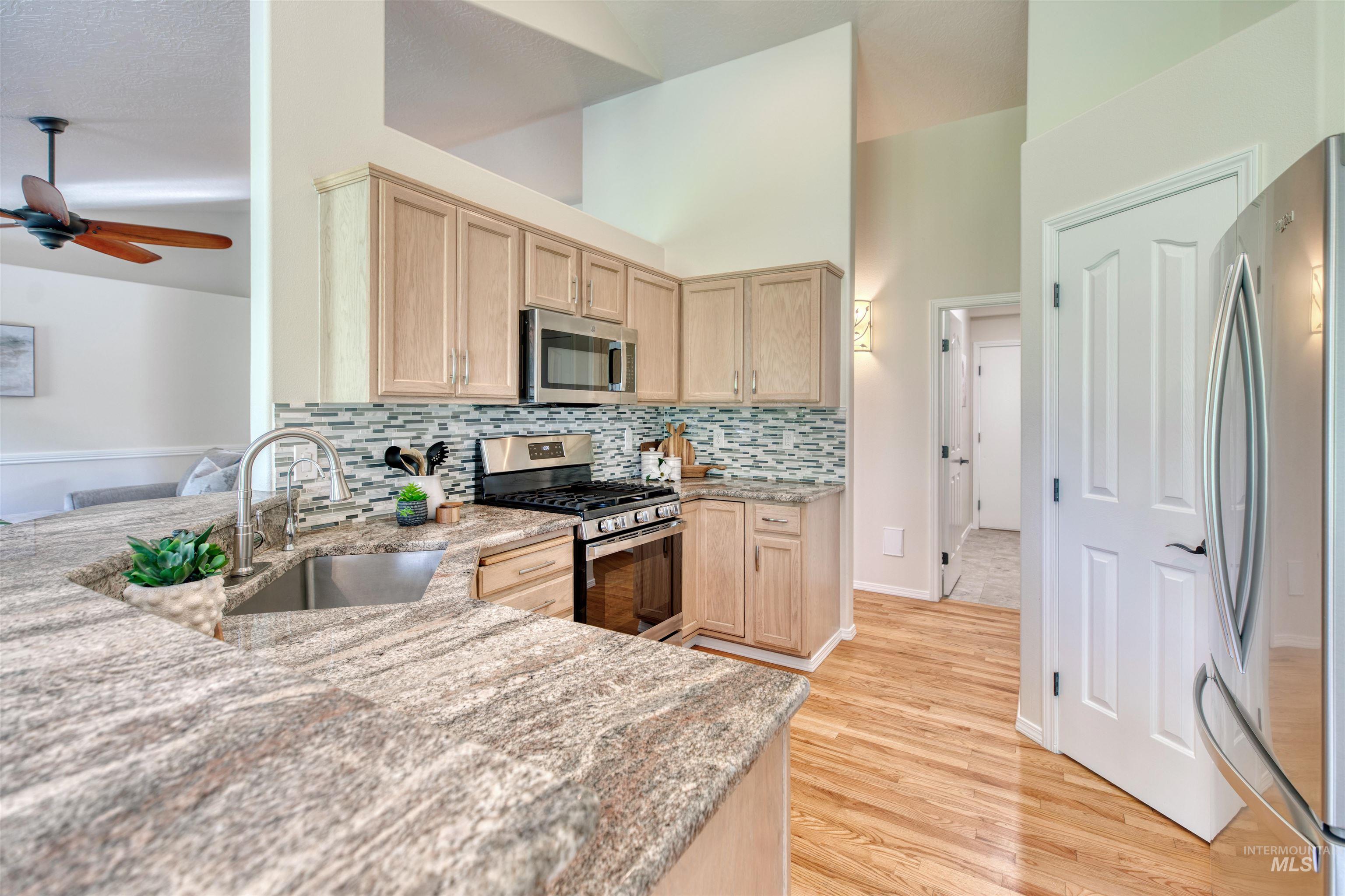 Kitchen with light brown cabinetry, stainless steel appliances, decorative backsplash, light stone countertops, and light wood finished floors