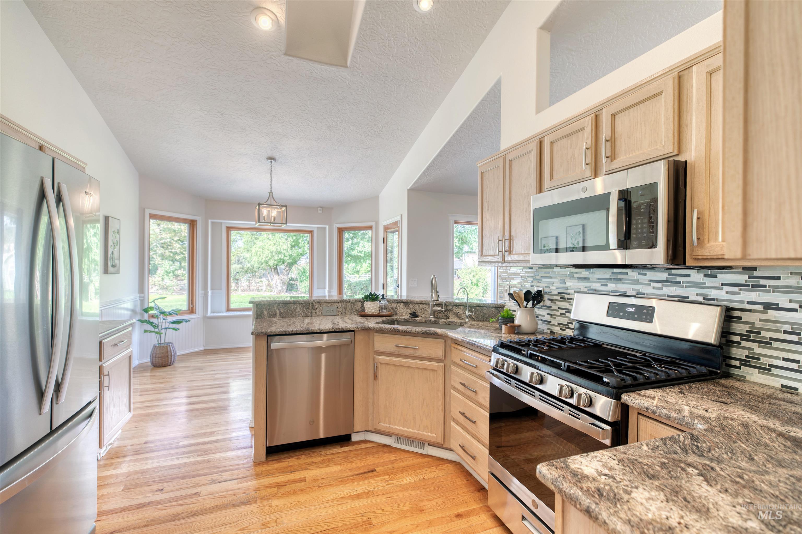 Kitchen featuring light brown cabinetry, appliances with stainless steel finishes, a textured ceiling, light wood finished floors, and a peninsula