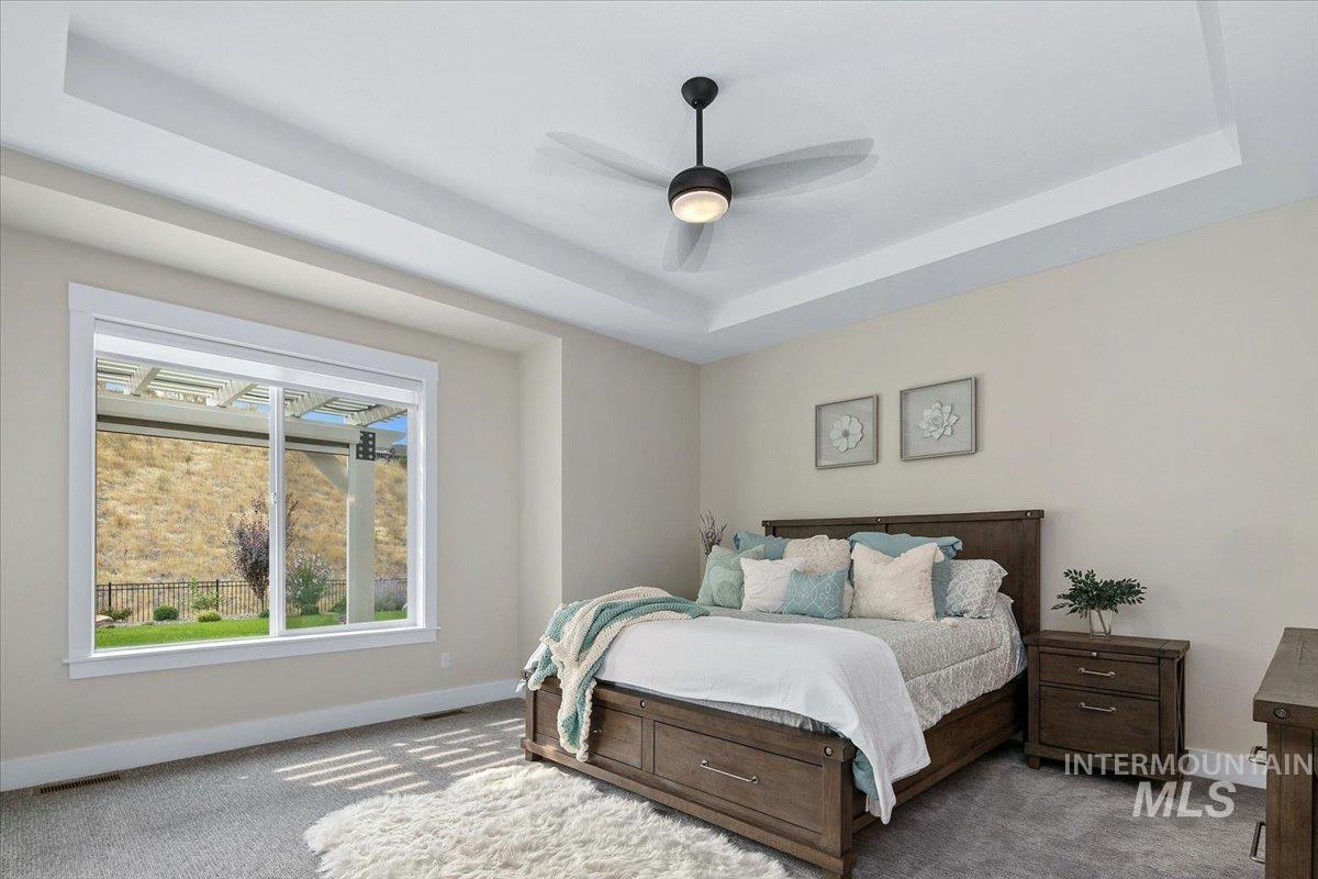 Carpeted bedroom with a tray ceiling and a ceiling fan