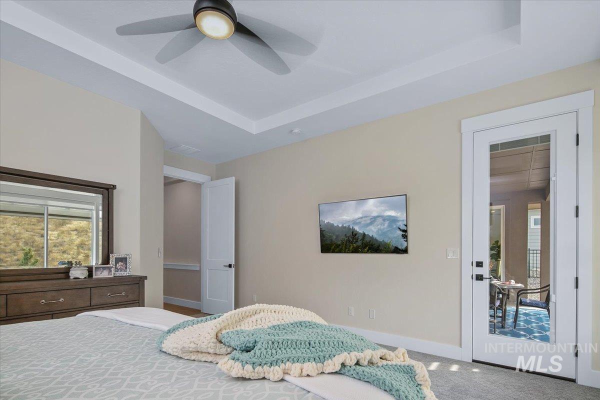 Carpeted bedroom featuring a raised ceiling and a ceiling fan