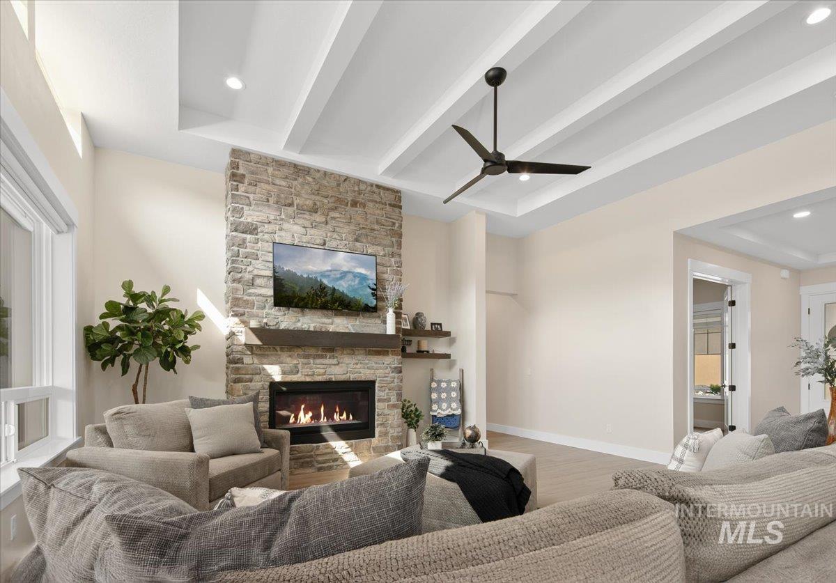 Living area with beam ceiling, wood finished floors, ceiling fan, recessed lighting, and a stone fireplace