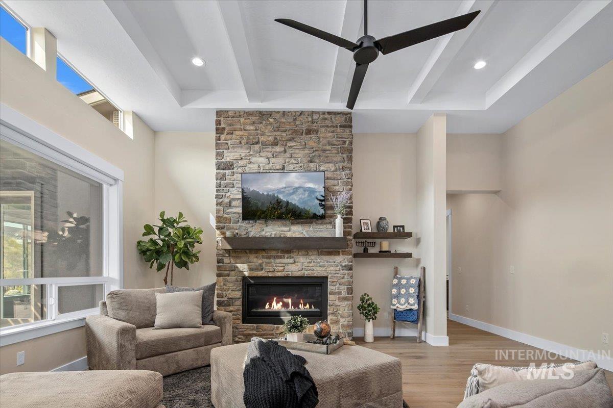 Living room featuring beamed ceiling, wood finished floors, and a stone fireplace