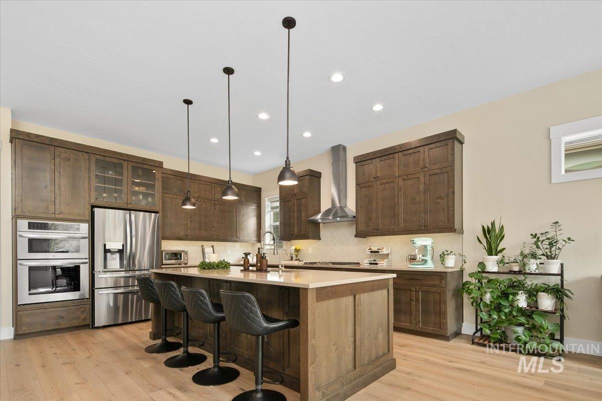Kitchen with appliances with stainless steel finishes, a breakfast bar, a kitchen island with sink, decorative light fixtures, and decorative backsplash