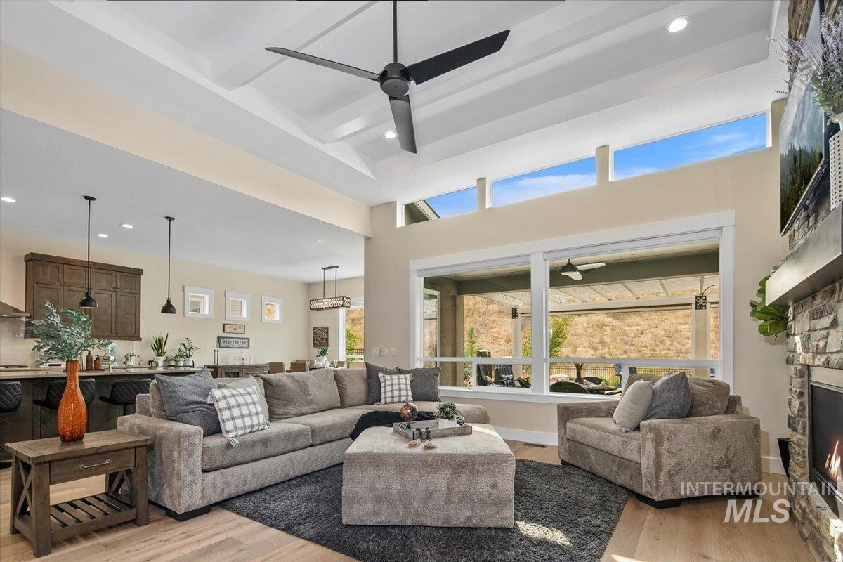 Living room with ceiling fan, light wood finished floors, recessed lighting, beamed ceiling, and a stone fireplace
