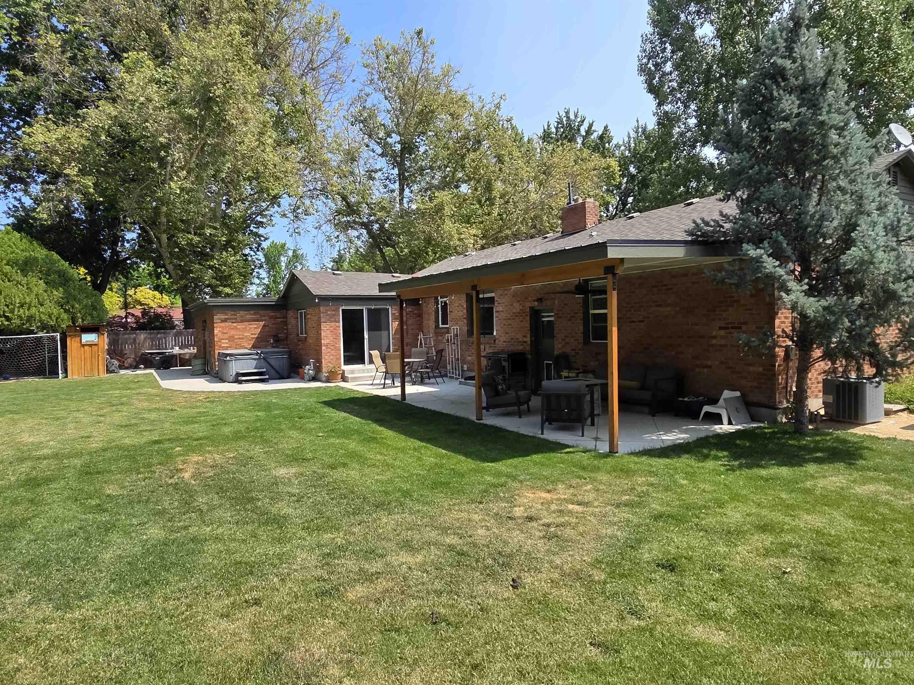 Rear view of house with a hot tub, a patio, brick siding, and a chimney