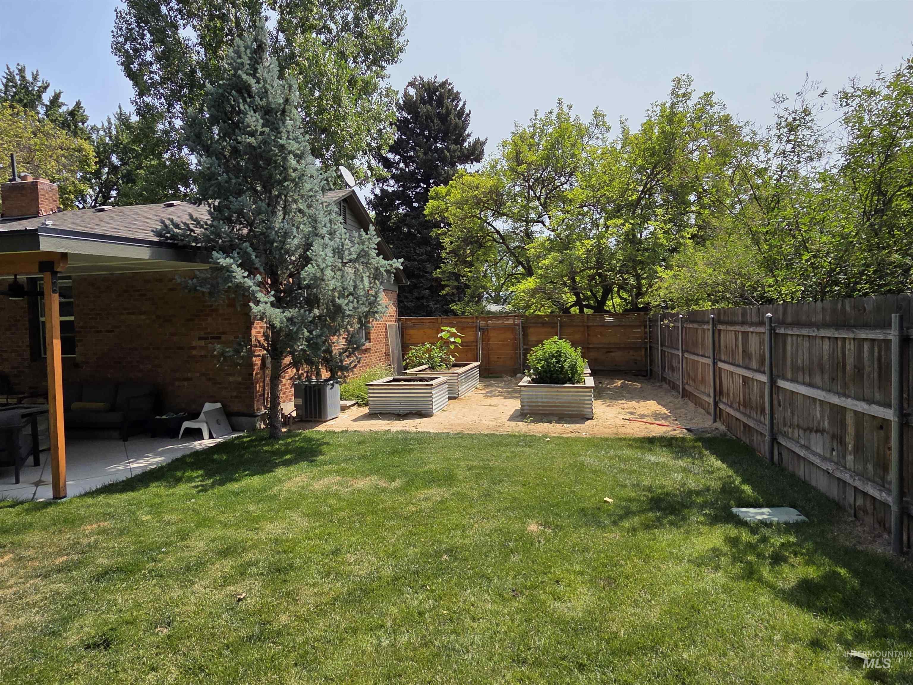 Fenced backyard with a vegetable garden and a patio area