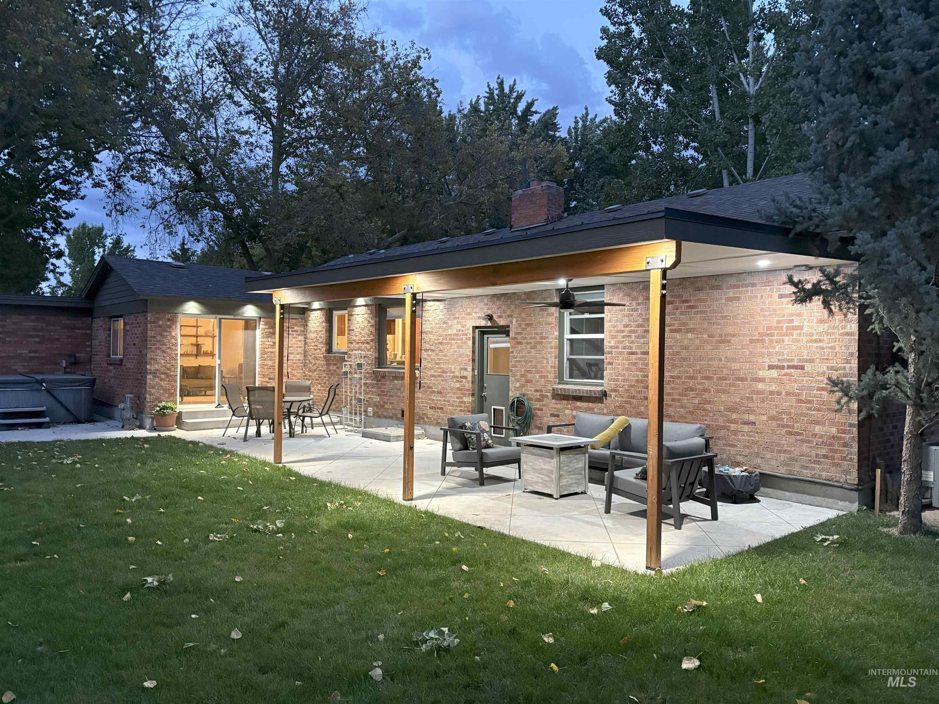 Back of house with a yard, a hot tub, a patio, brick siding, and a chimney