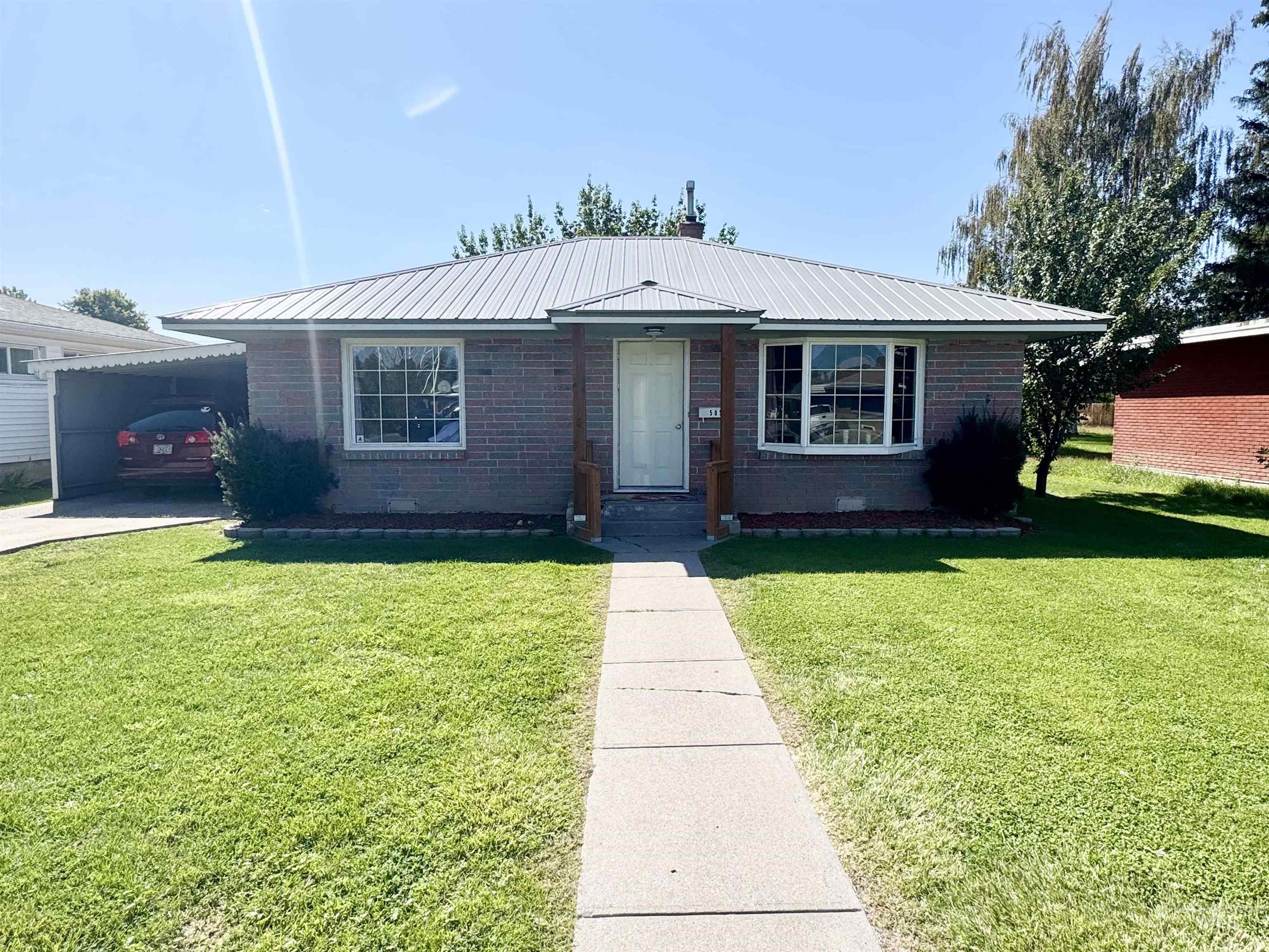 Single story home with a metal roof, a front yard, and brick siding