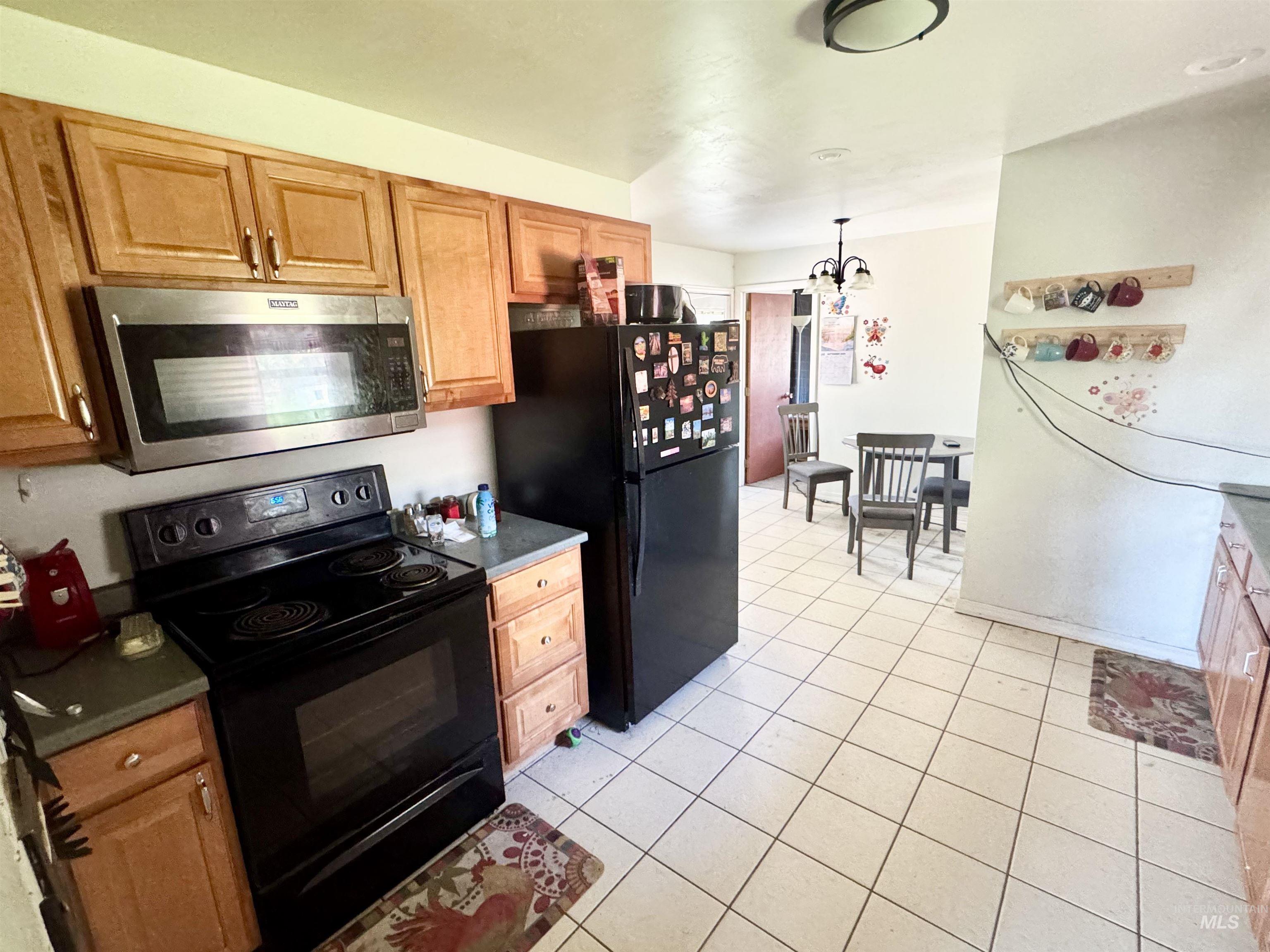 Kitchen featuring black appliances, light tile patterned floors, dark countertops, hanging light fixtures, and a chandelier