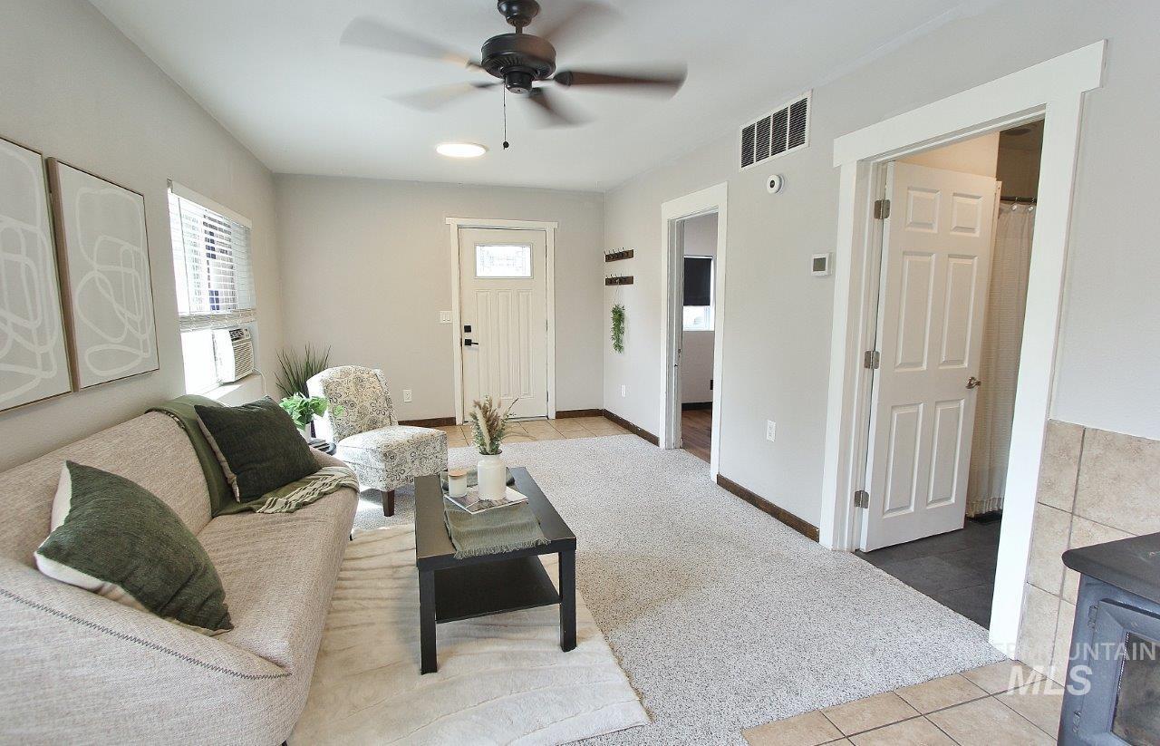 Living room with light tile patterned flooring, light colored carpet, a ceiling fan, and a wood stove
